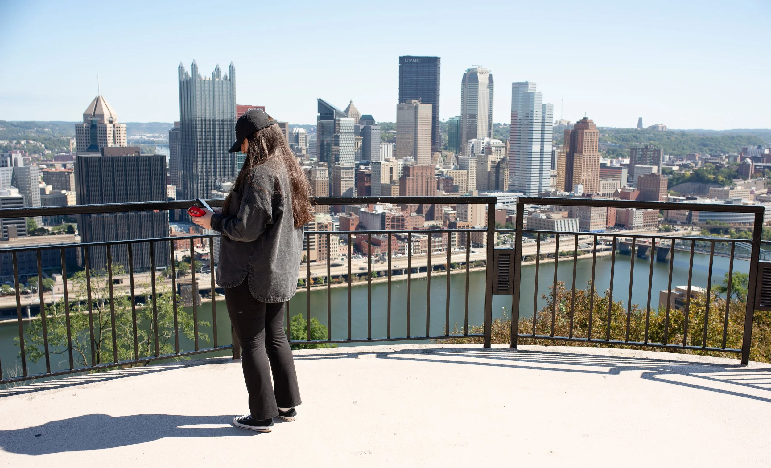 Person standing at Grandview Overlook looking out over the Pittsburgh skyline and river on a clear morning.