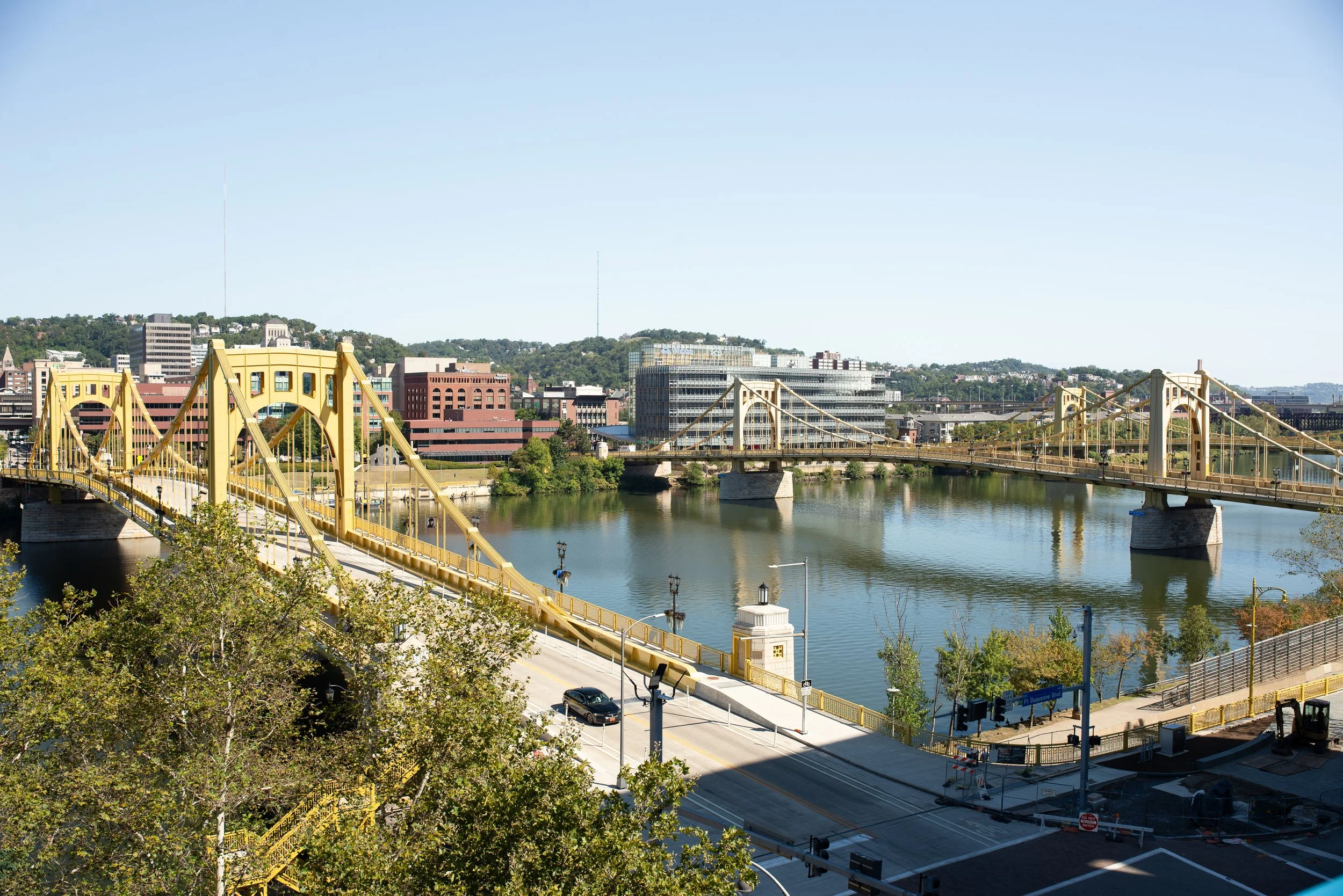 View of Pittsburgh’s yellow bridges spanning the river, seen from a downtown parking deck with the city skyline and calm water below.