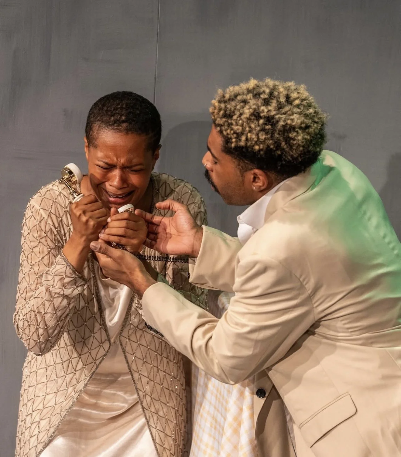 A woman crying and clutching a telephone, while a man in a beige suit comforts her.
