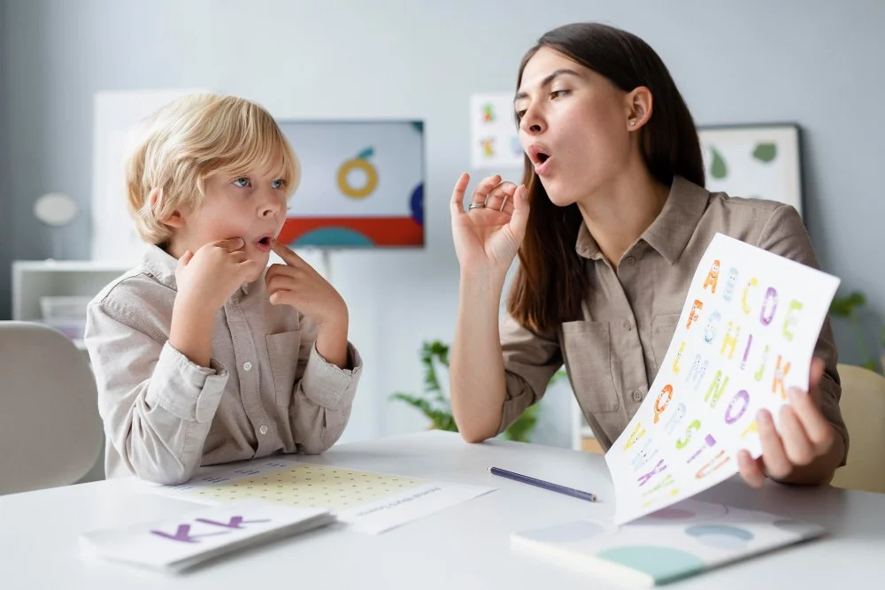 A young woman instructor teaching a boy child about the alphabet during a literacy lesson in a classroom.