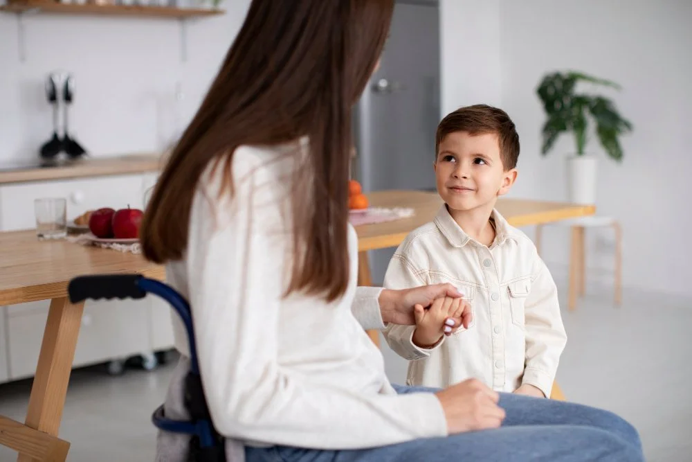 A young boy holding hands with a woman in a wheelchair in a bright kitchen.