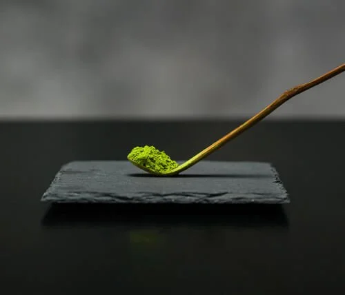 Thé vert Matcha de Cérémonie HISUI biologique sur une cuillère de bois traditionnelle posée sur une ardoise noire.