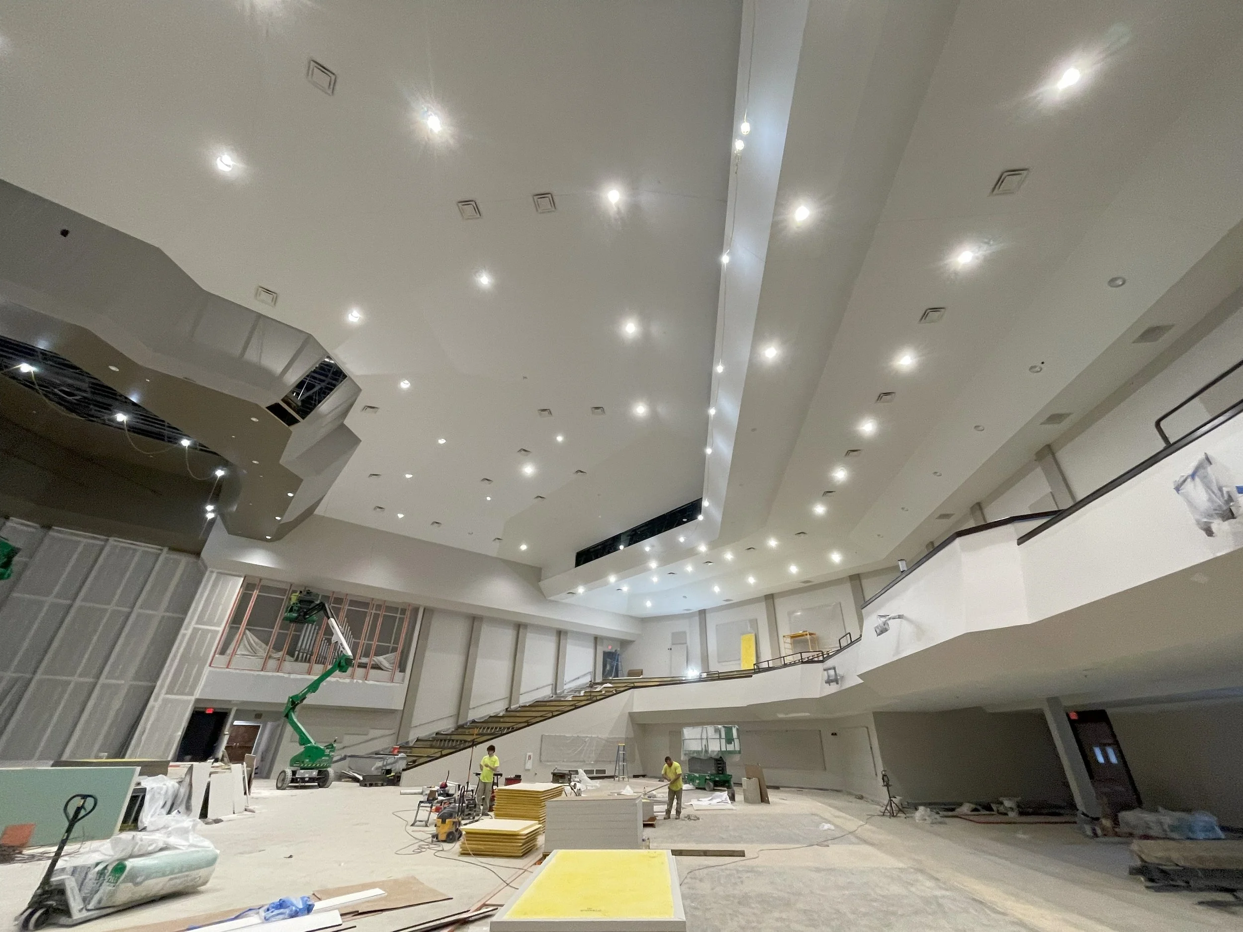 Interior of a large building under construction with workers, scaffolding, and construction materials.