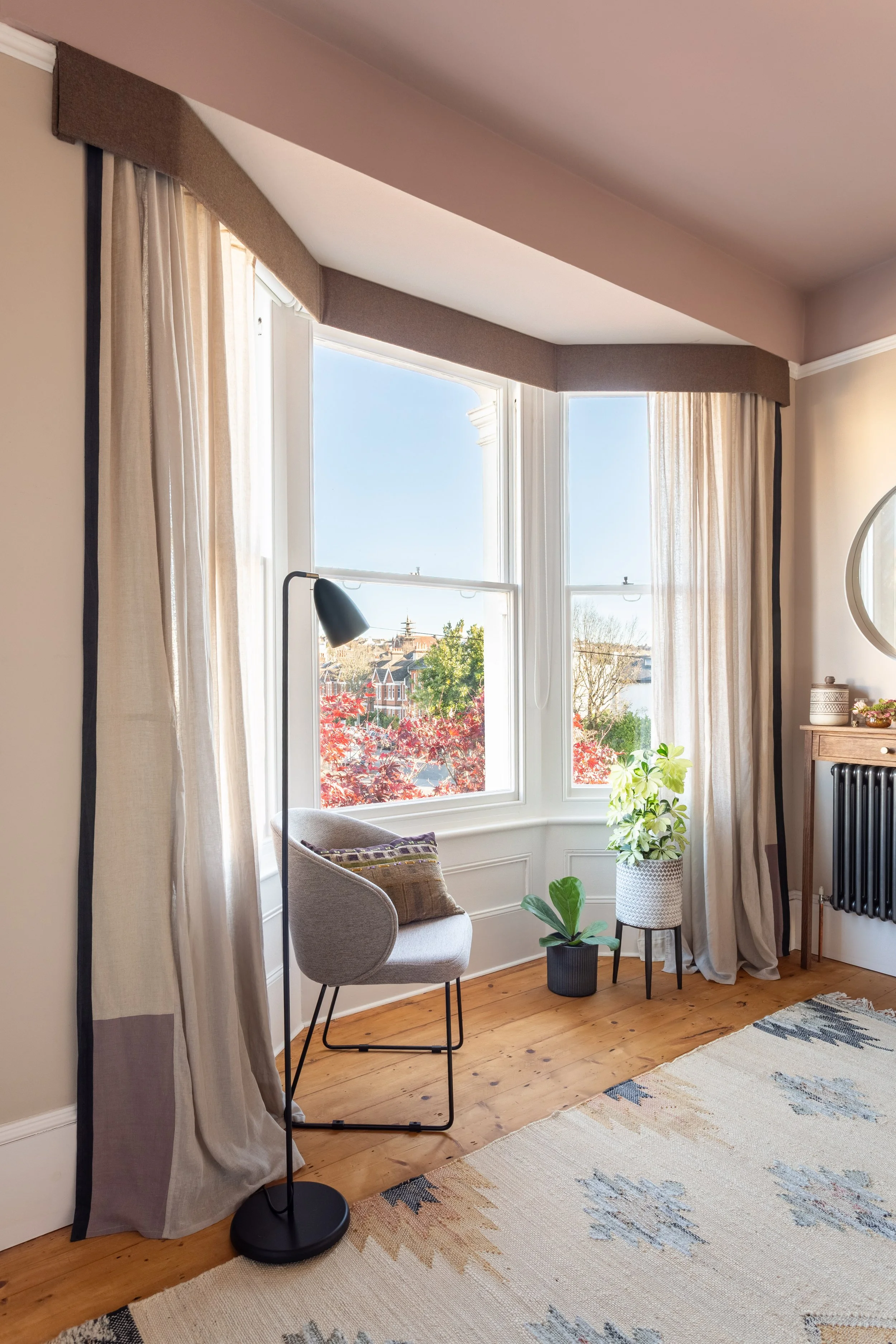 Elegant bedroom with warm neutral colour palette, bespoke built in wardrobe, light muslin curtains, wooden flooring and contemporary lighting.