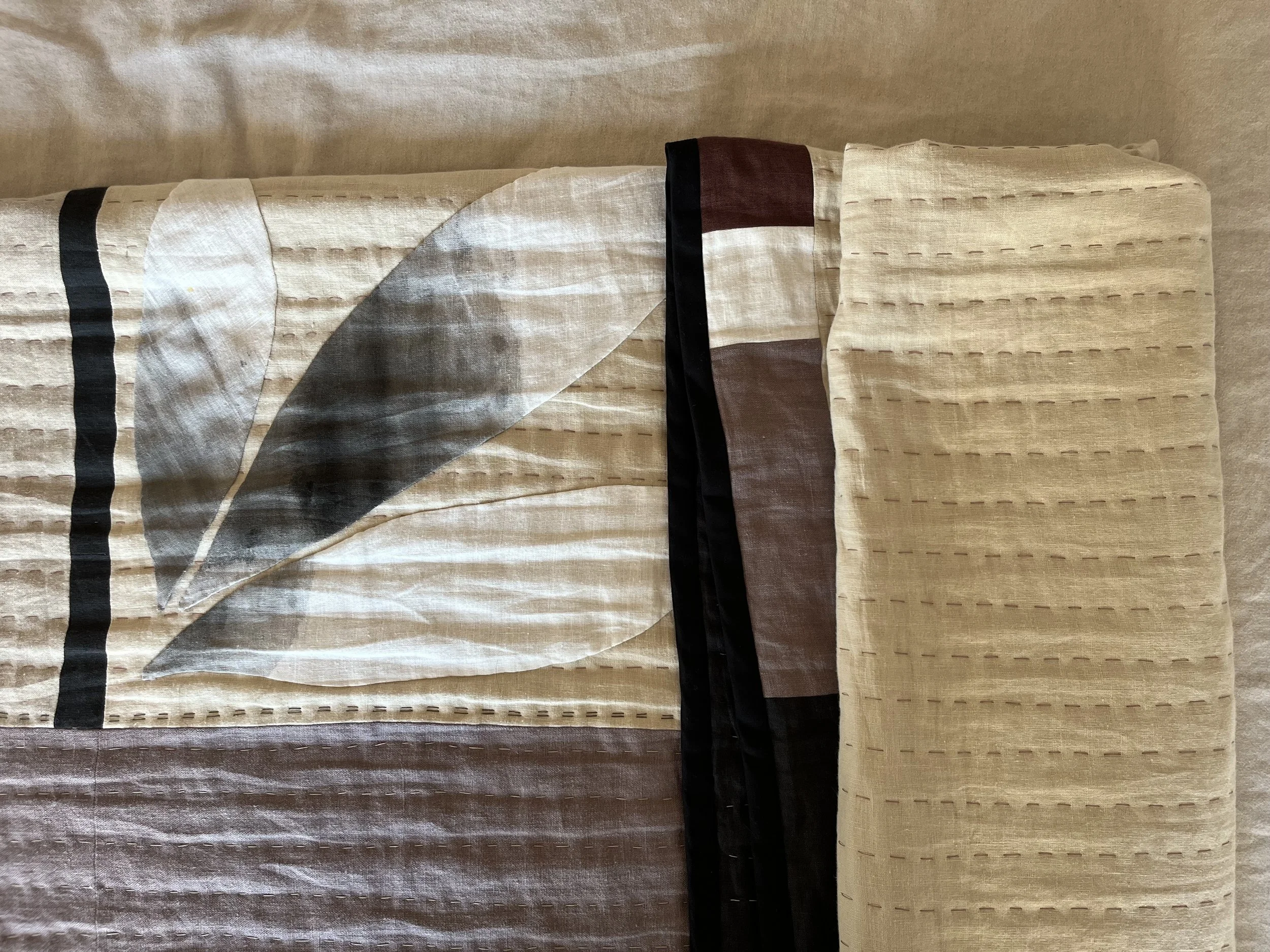 lose up detail of handmade linen quilted and appliquéd bedspread in neutral colours with bold black accents.