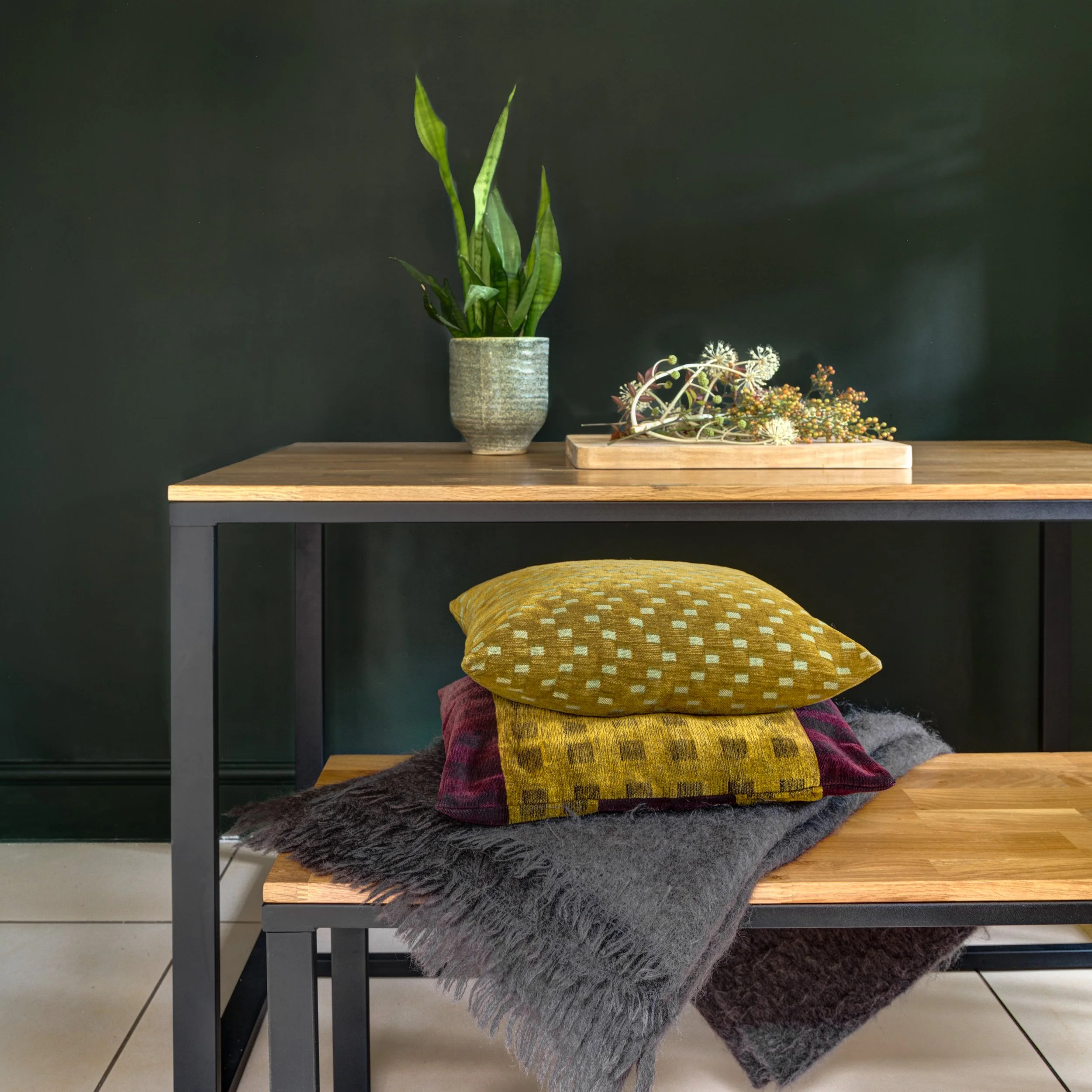 Handmade cushions on a dining table bench in front of rich dark green wall.