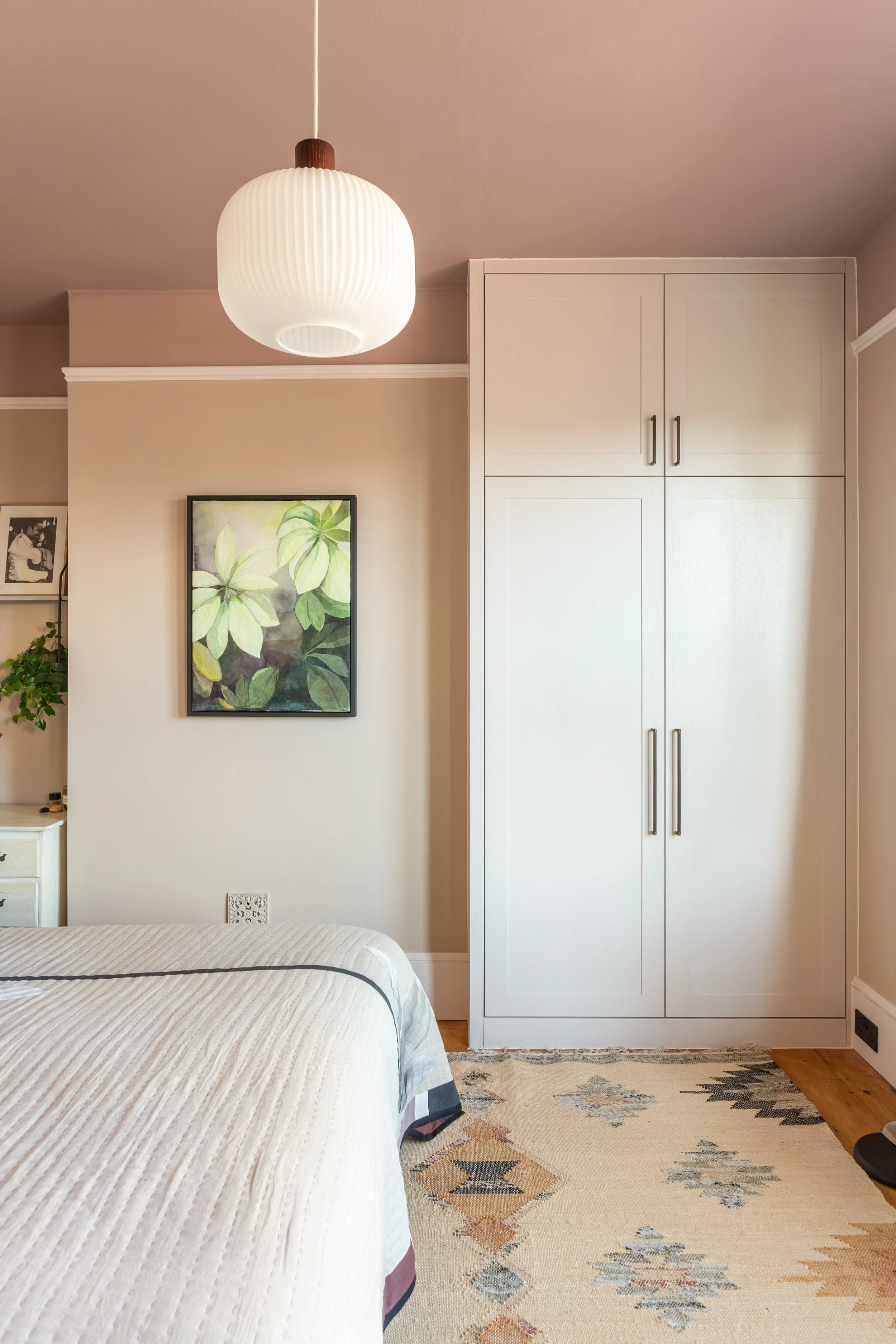 Elegant bedroom with warm neutral colour palette, bespoke built in wardrobe, bespoke textile framed artwork, wooden flooring and contemporary lighting.