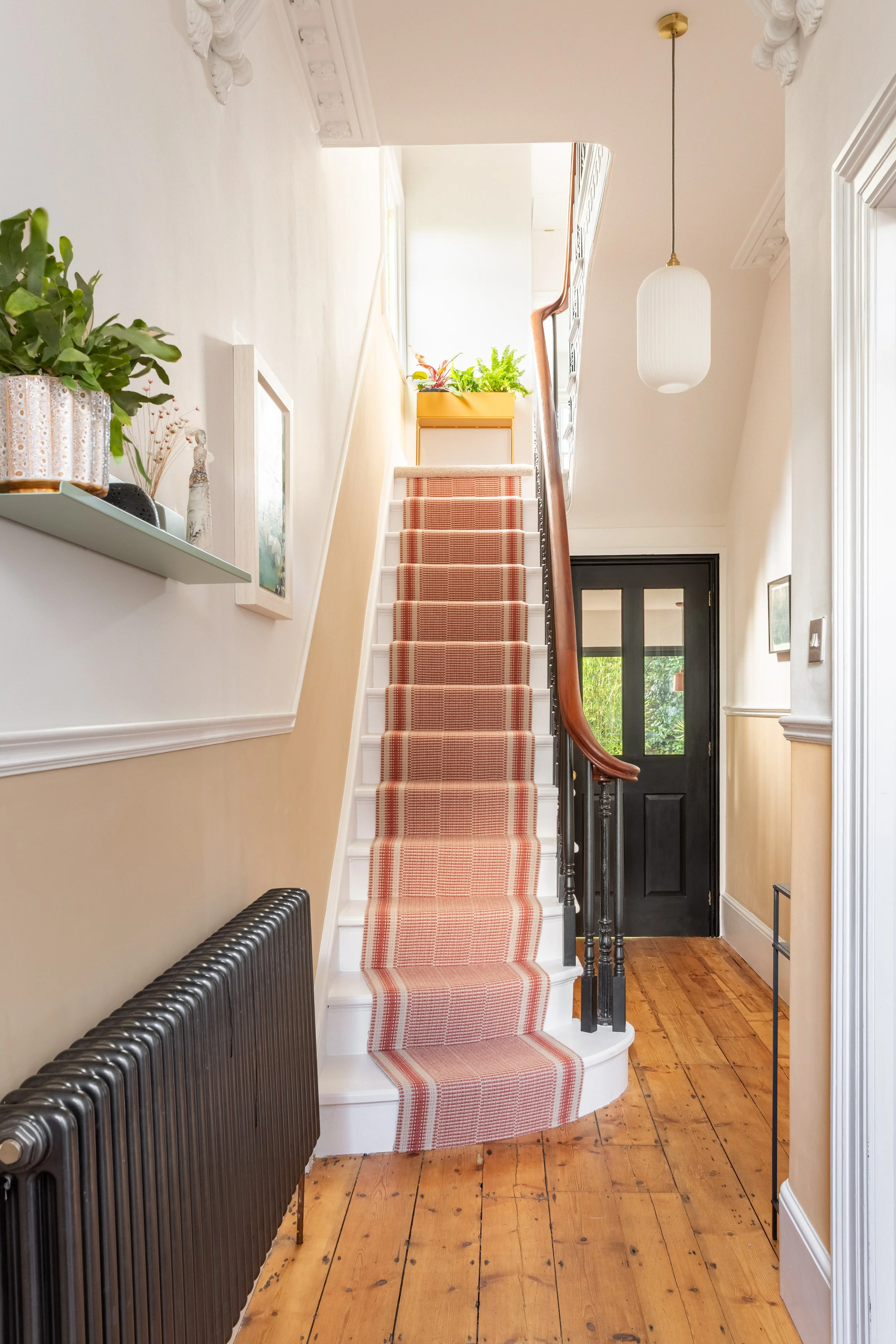Entrance hall showing a staircase in a Victorian home with a Roger Oates Mila terracotta runner. The hallway has the original wooden floors, a warm, neutral colour palette with bold accents, styled floating shelf and artwork.