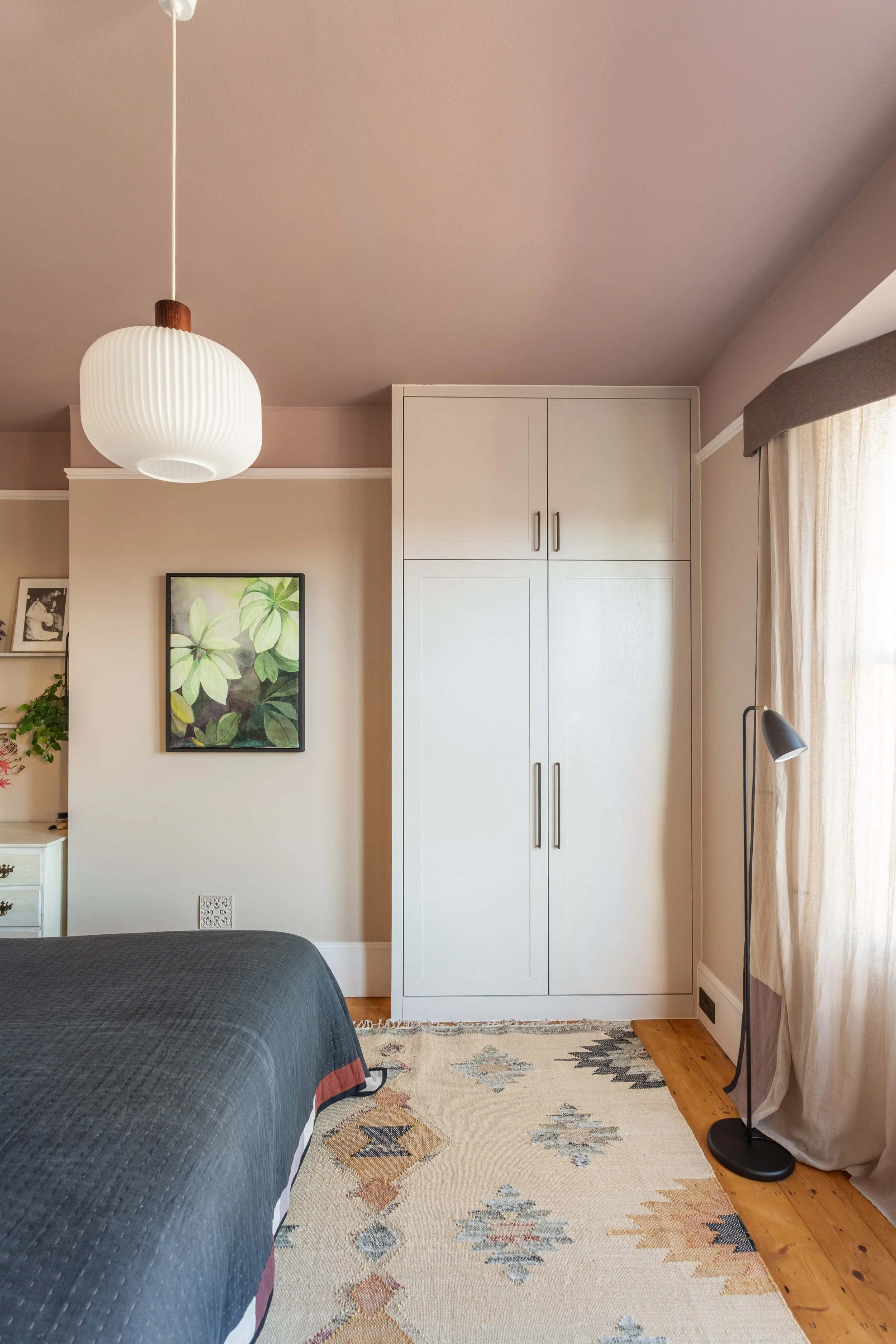 Elegant bedroom with warm neutral colour palette, bespoke built in wardrobe, light muslin curtains, wooden flooring and contemporary lighting.