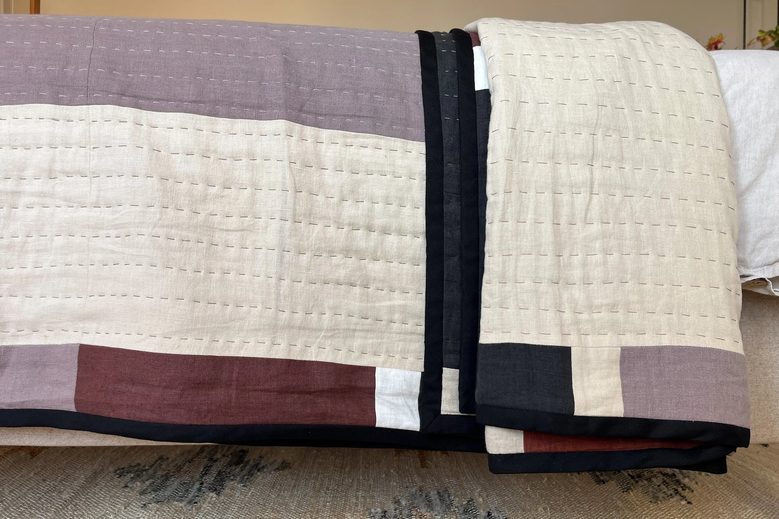 Close up detail of handmade linen quilted and appliquéd bedspread in neutral colours with bold black accents.