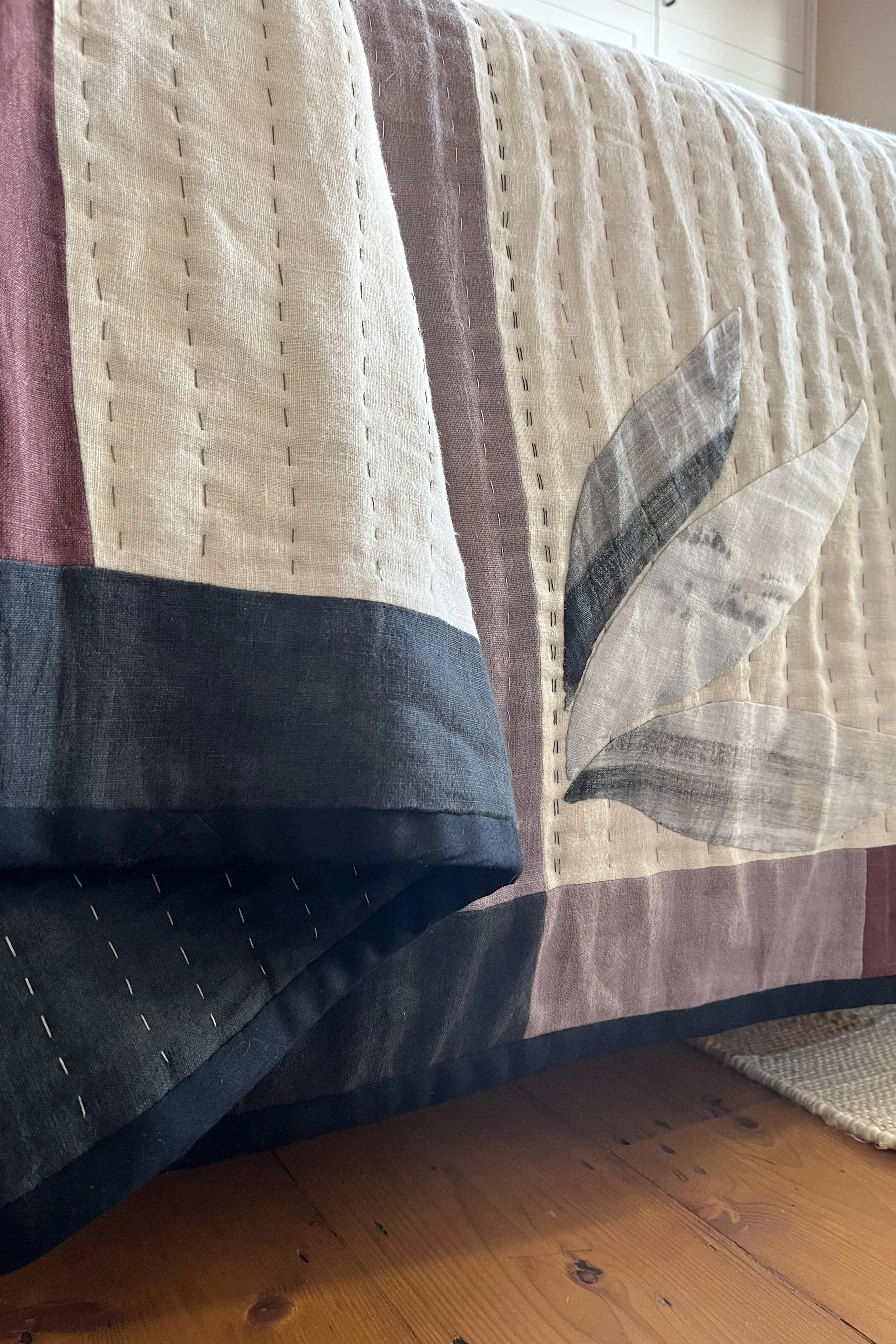 Close up detail of handmade linen quilted bedspread in neutral colours with bold black accents.