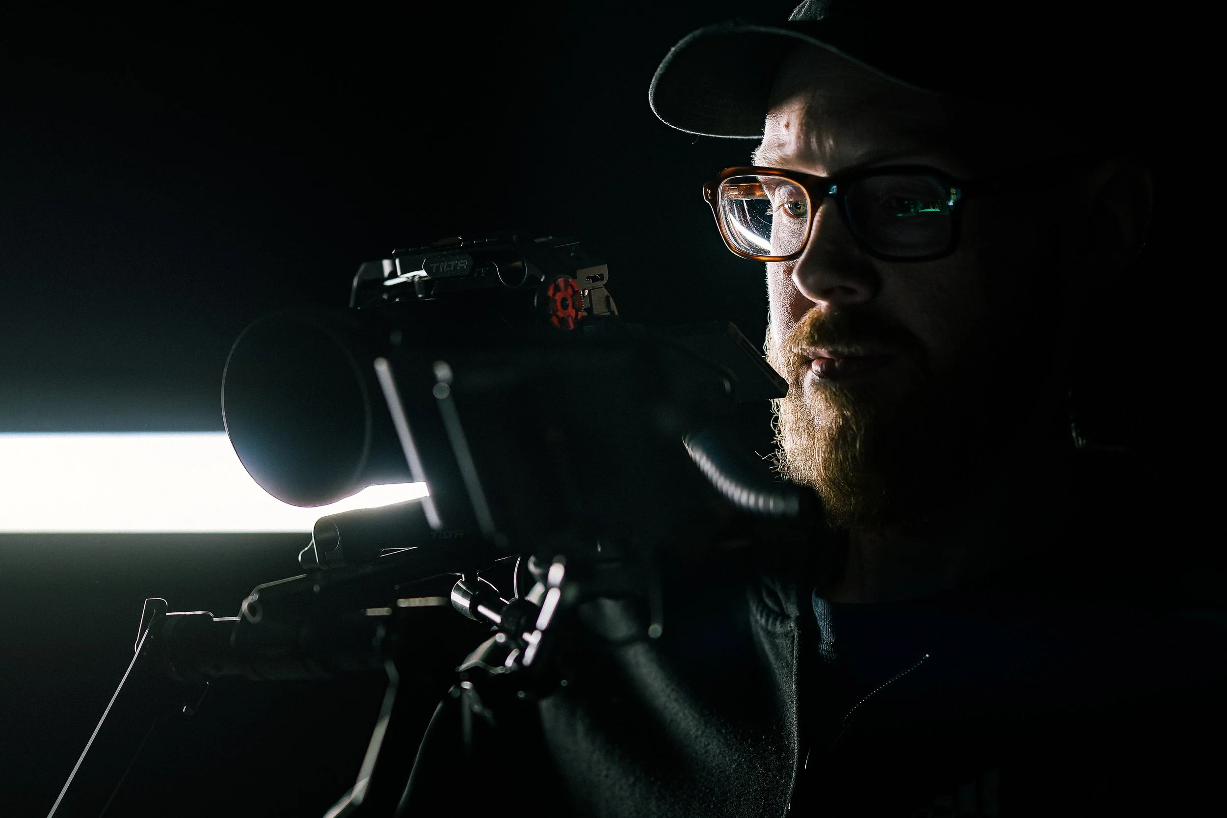 Half illuminated Man with glasses operating film camera in the darkness.