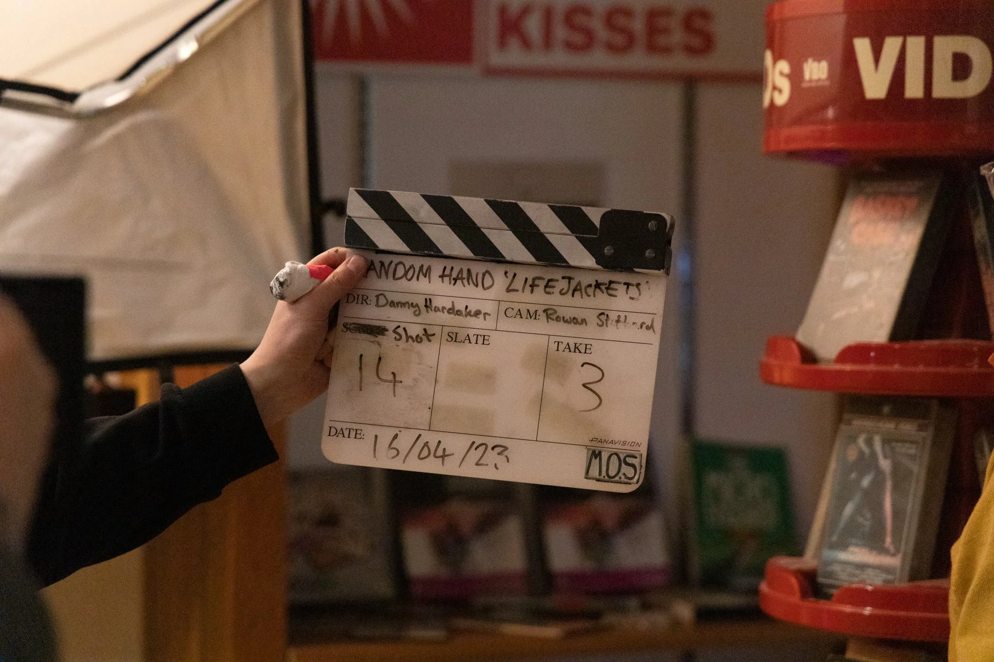 A person holding a film slate labeled 'Random Hand Lifejackets' in a setting that appears to be a film set or production area.