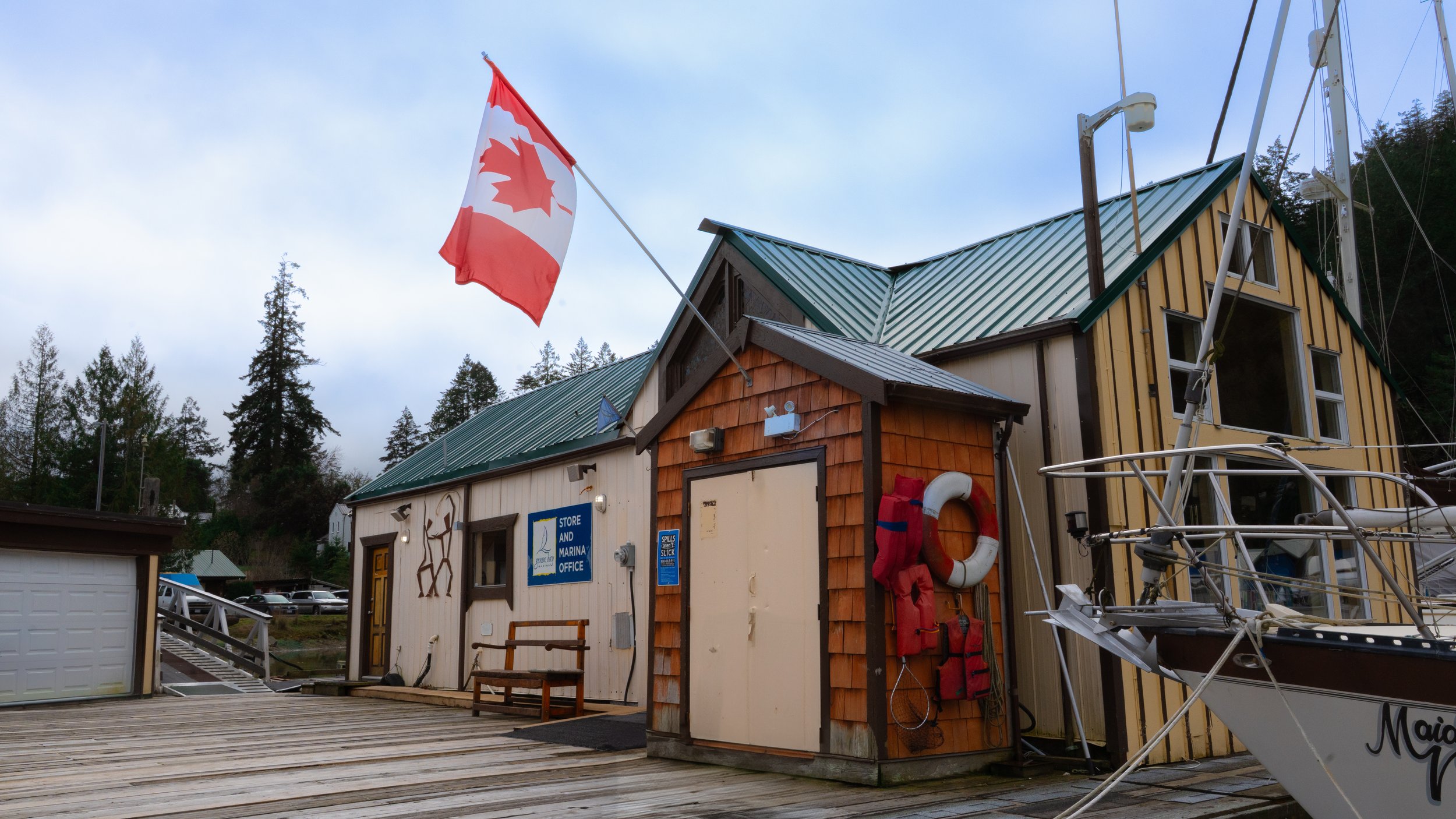 A marina building with a Canadian flag, life jackets, and a lifebuoy on the wall, boat dock, surrounded by trees.
