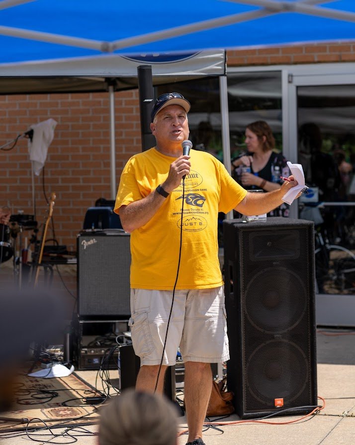 Man in yellow shirt speaking into microphone outdoors