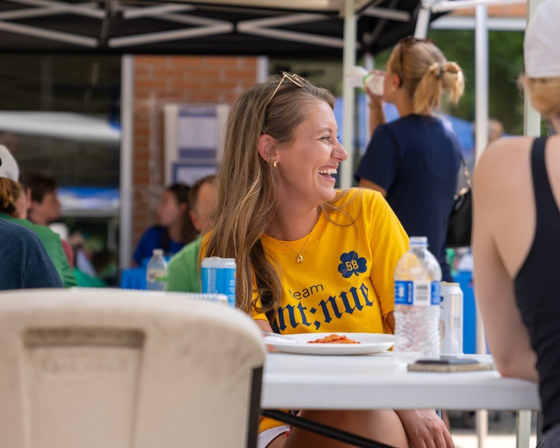 Group of people sitting outdoors at a table with drinks, a woman in a yellow shirt laughing.