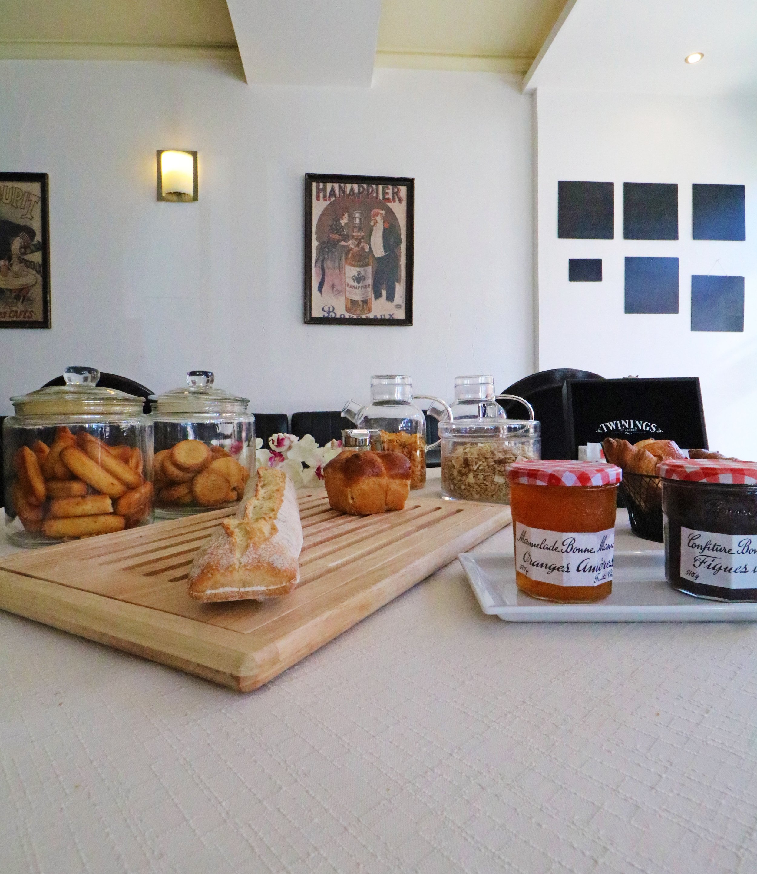 Un petit déjeuner avec baguette de pain, pots de confiture, viennoiseries et biscuits dans des bocaux en verre, avec des affiches rétro sur le mur.