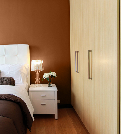Chambre avec lit, table de chevet, lampe, vase avec fleurs, armoire en bois
