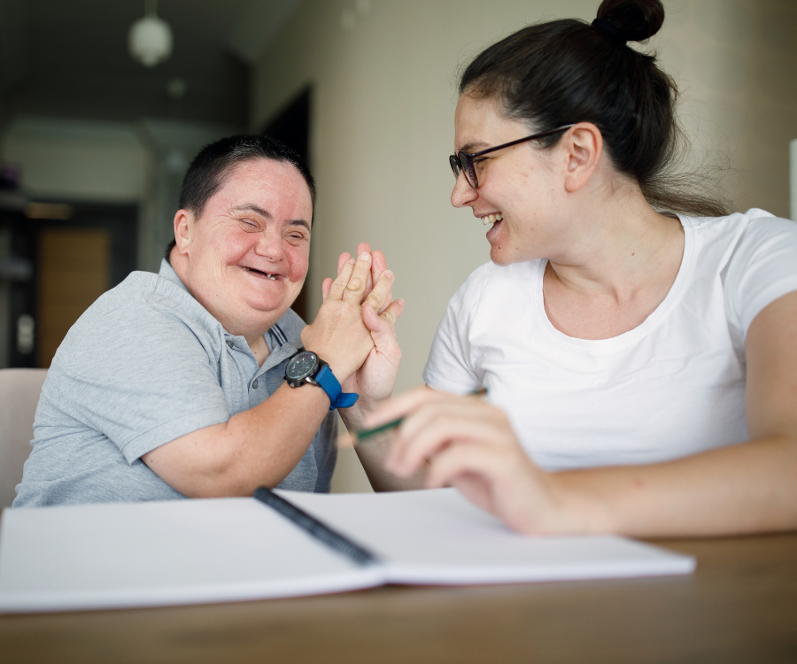 Woman high fives a person with disabilities after they work over a written assignment on a desk.