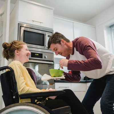 Man feeding a woman in a wheelchair in a kitchen