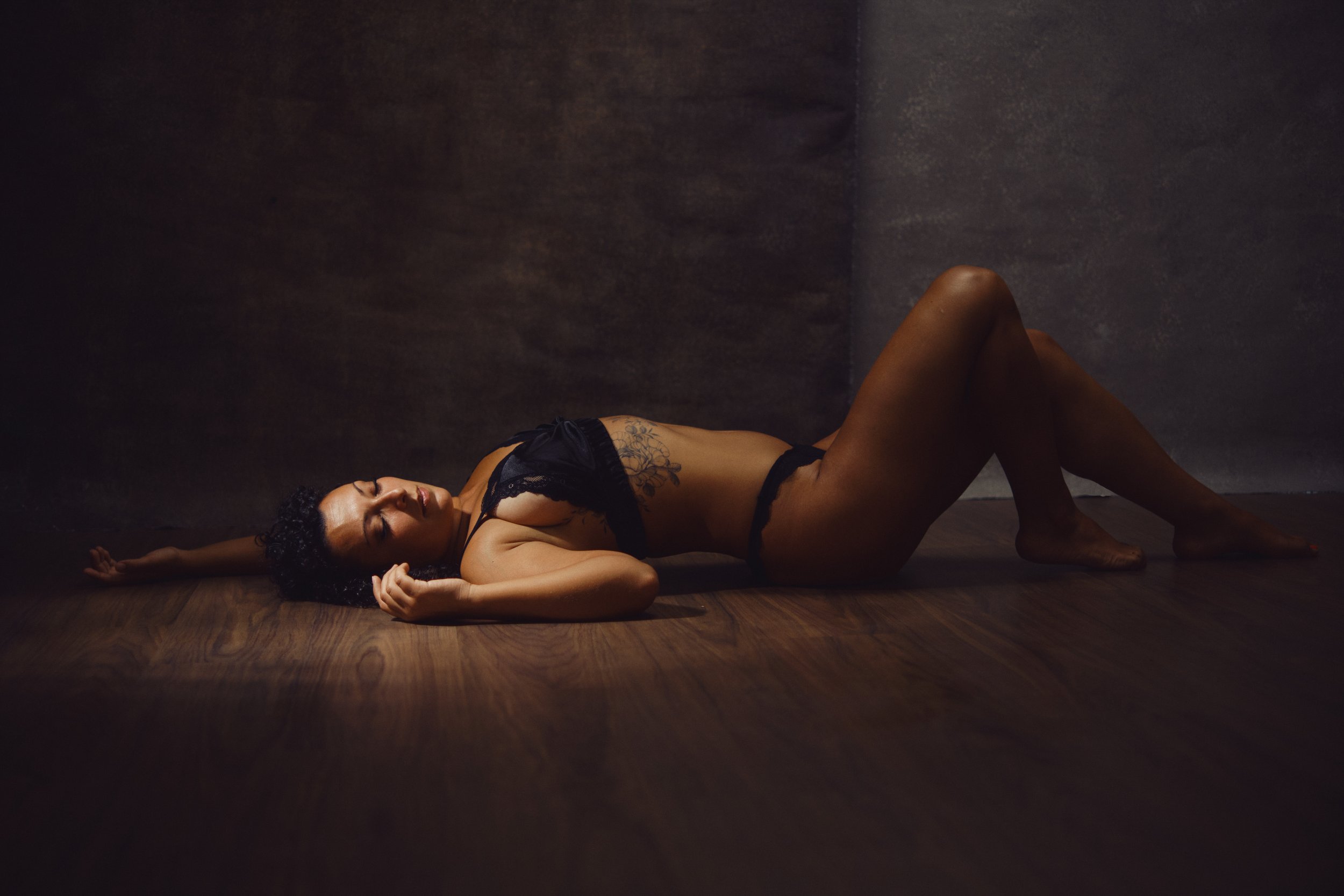 Mulher deitada no chão de madeira numa sessão fotográfica feminina intimista em Lisboa, lingerie preta e luz suave