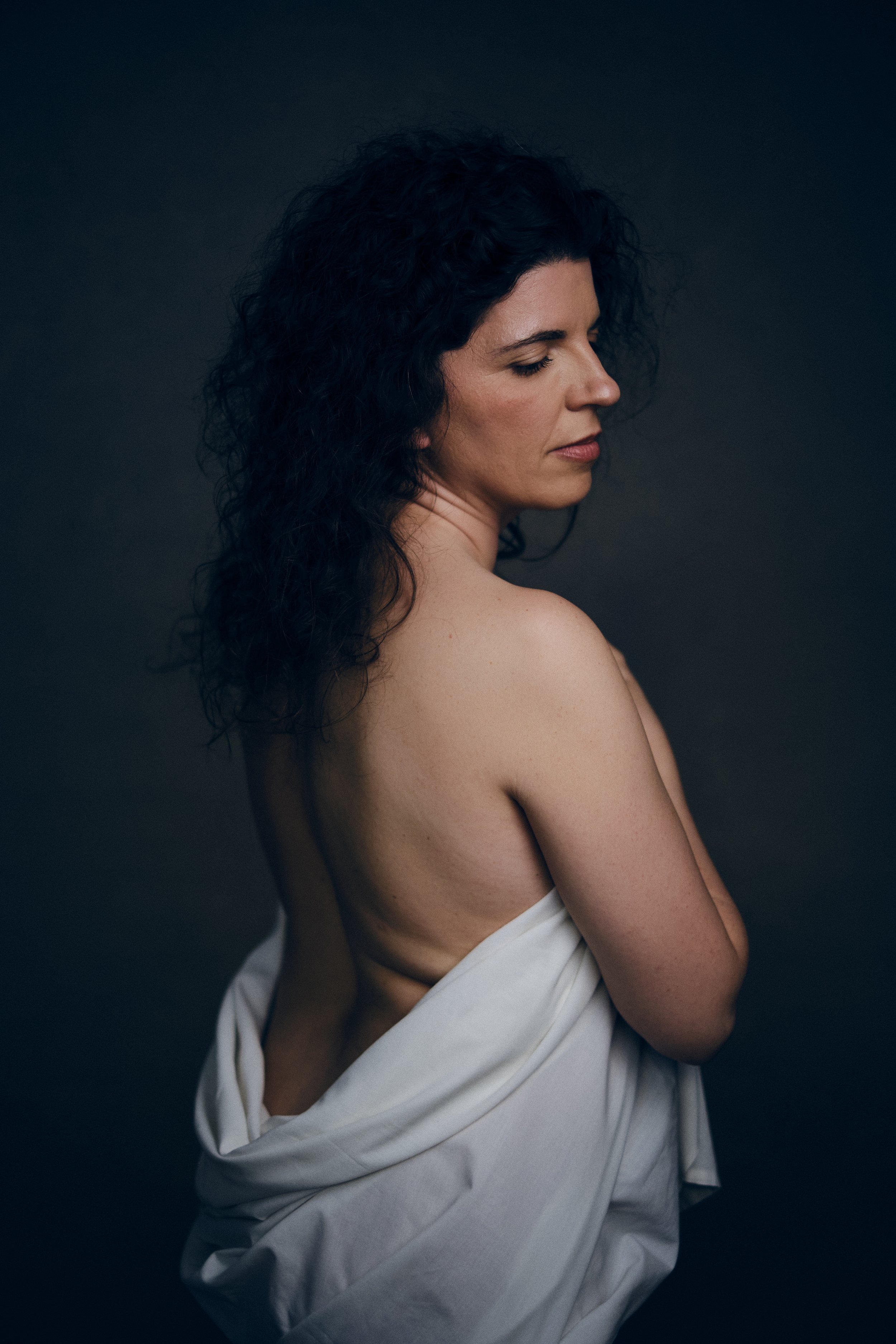 Mulher de cabelo encaracolado parcialmente envolta em tecido branco numa sessão fotográfica feminina intimista em Lisboa
