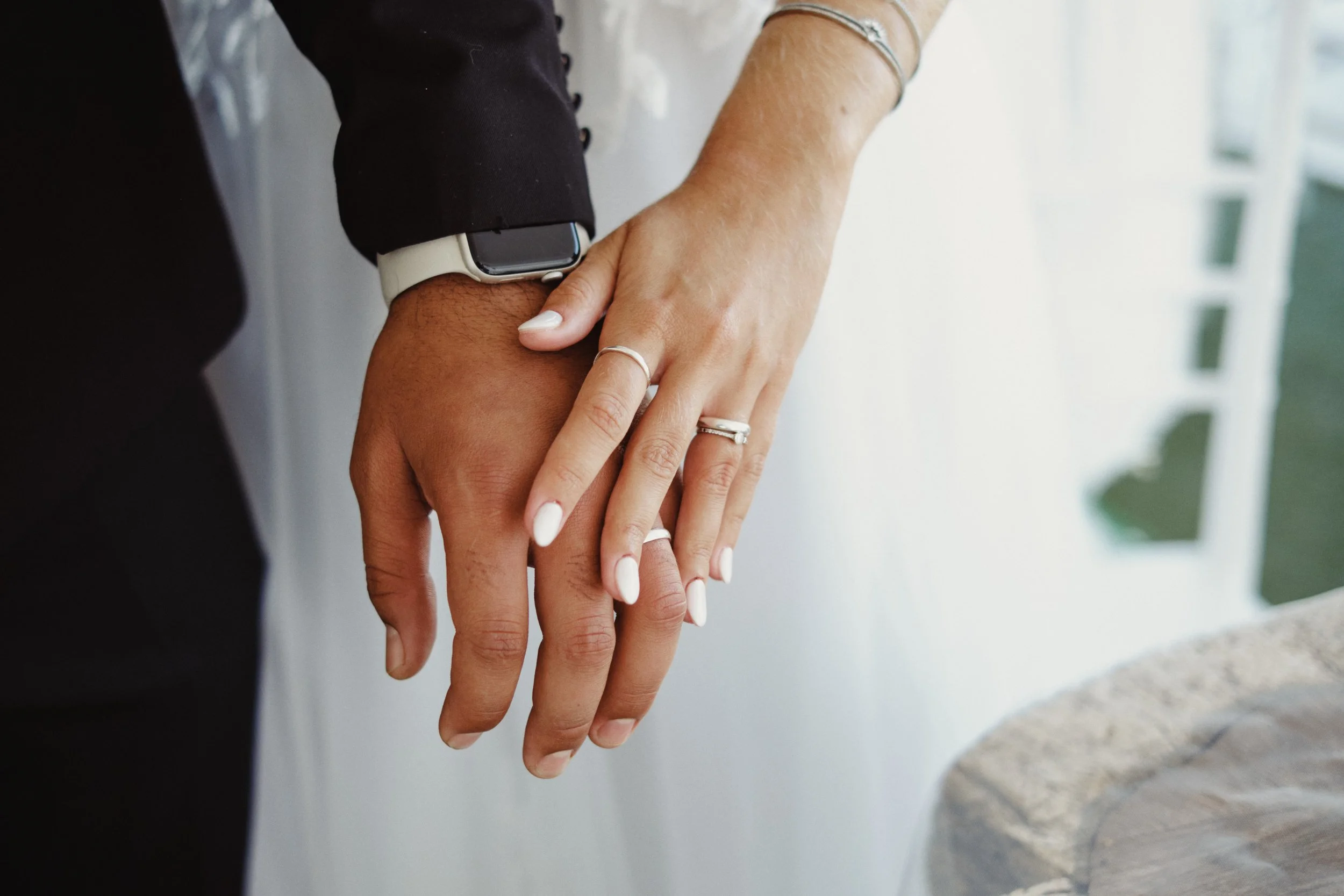 Fotografia documental de casamento em Lisboa, mãos de casal entrelaçadas, alianças visíveis e fundo desfocado