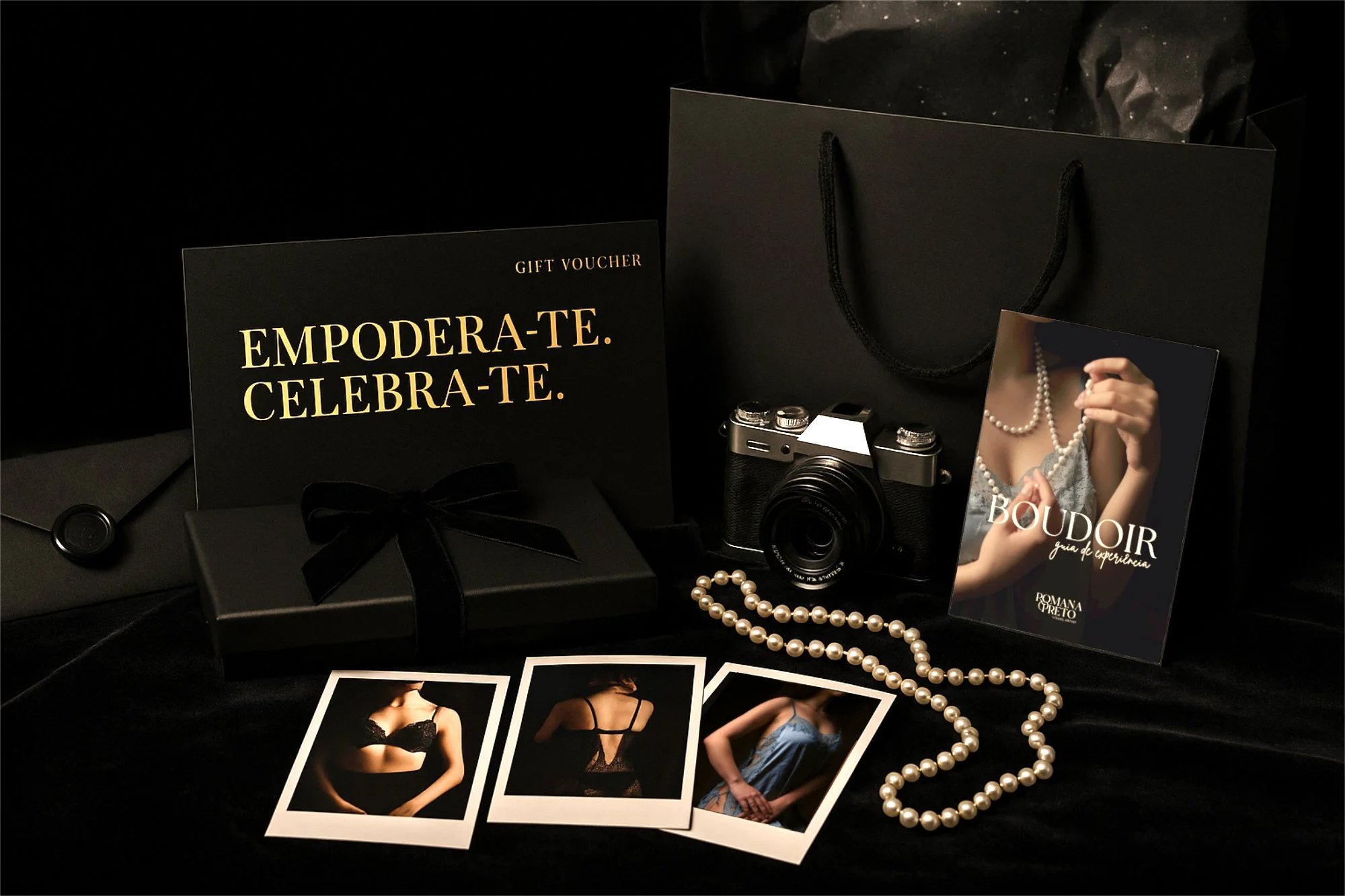 Boudoir gift set with black gift box, ribbon, pearl necklace, vintage camera, printed photos, gift voucher for boudoir session in Lisbon, and black shopping bag on dark fabric background.