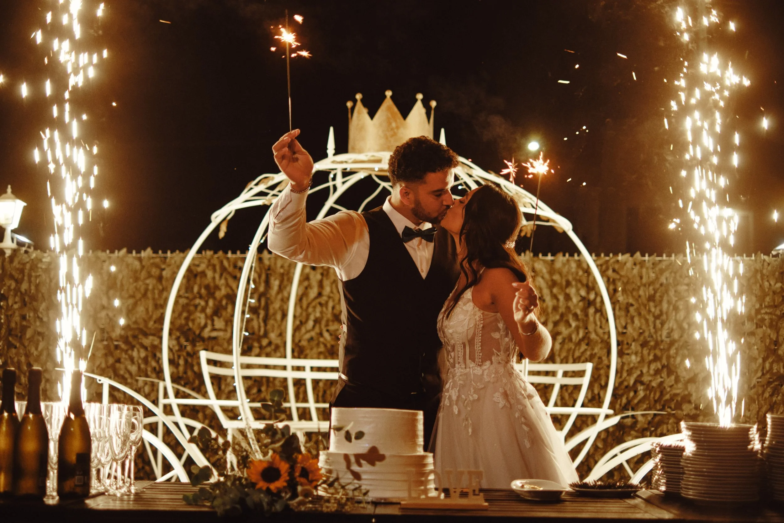 Fotografia artística de casamento em Lisboa, casal recém-casado a beijar-se durante a receção, iluminação quente e detalhes festivos