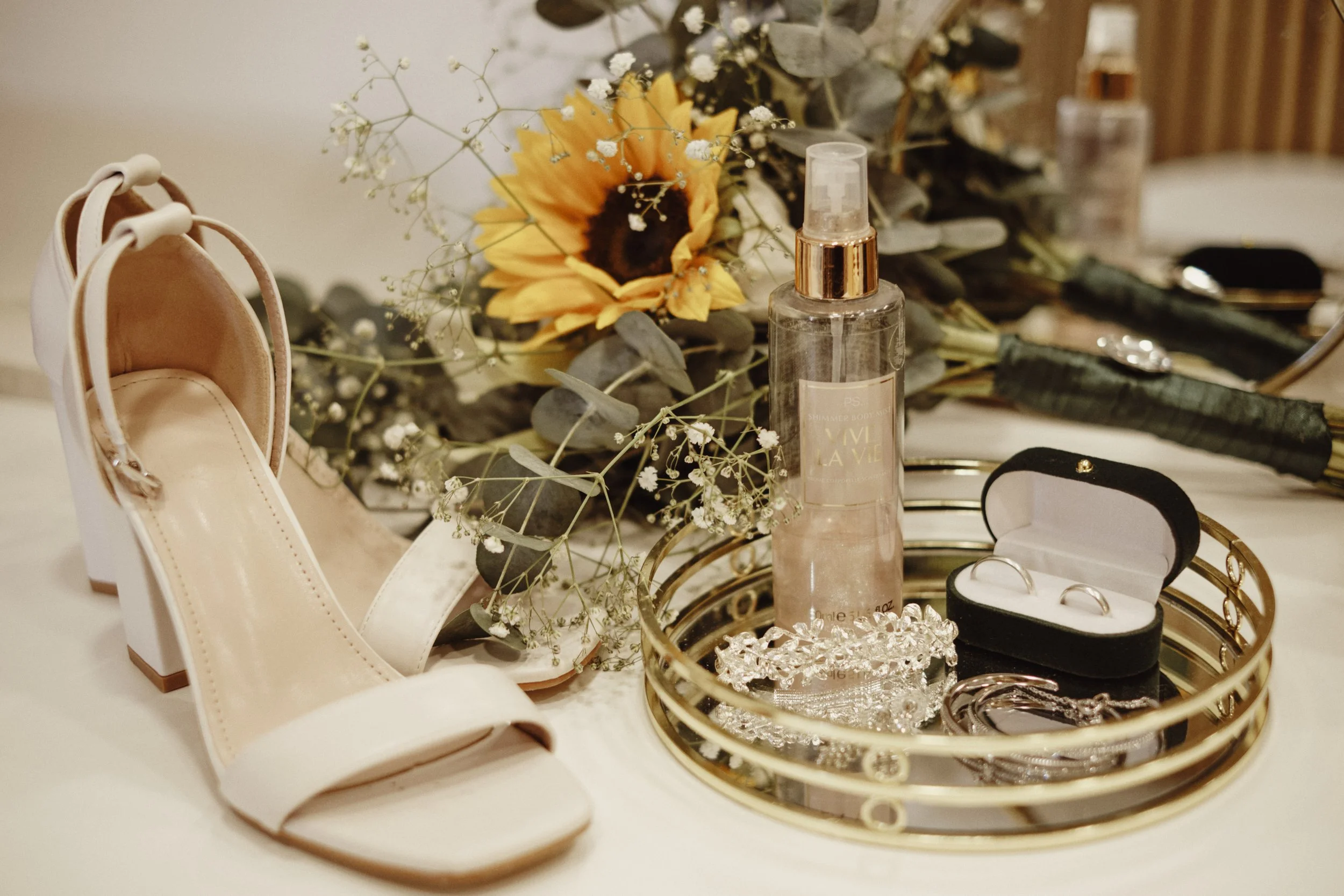 Fotografia artística de detalhes de casamento em Lisboa: sapatos de salto, joias, perfume e arranjo floral com girassol