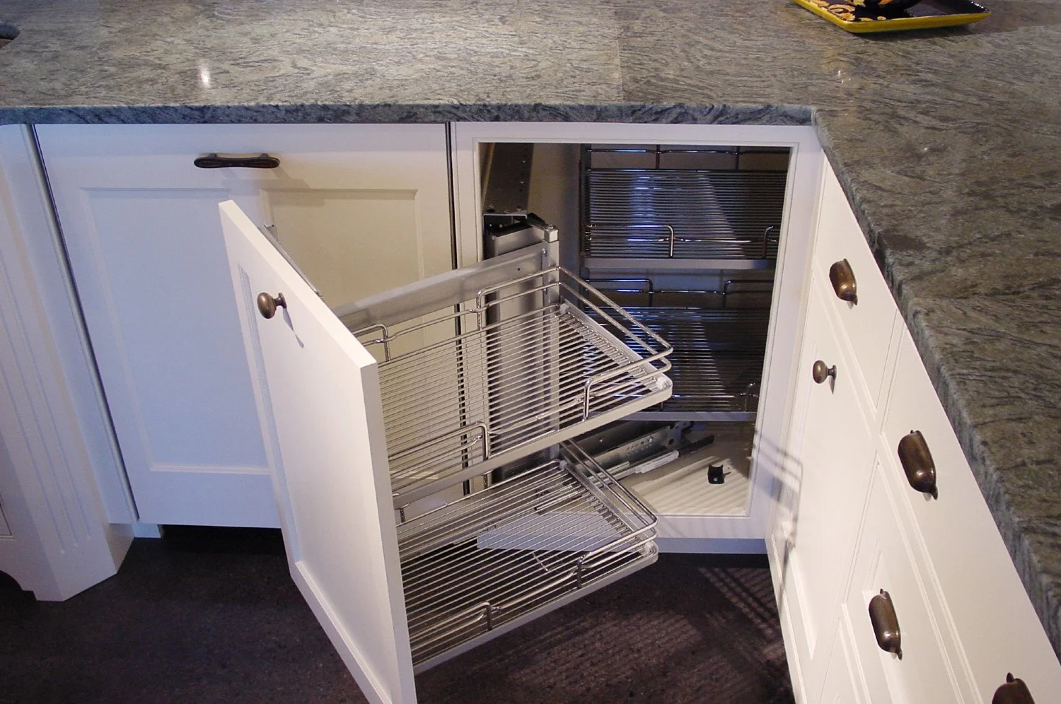 Open kitchen cabinet with empty pull-out wire shelves under a gray granite countertop.