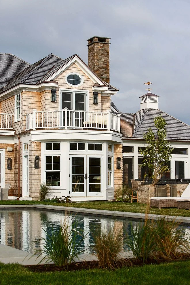 A large, elegant house with beige siding and white trim, a balcony, and a swimming pool in the backyard.