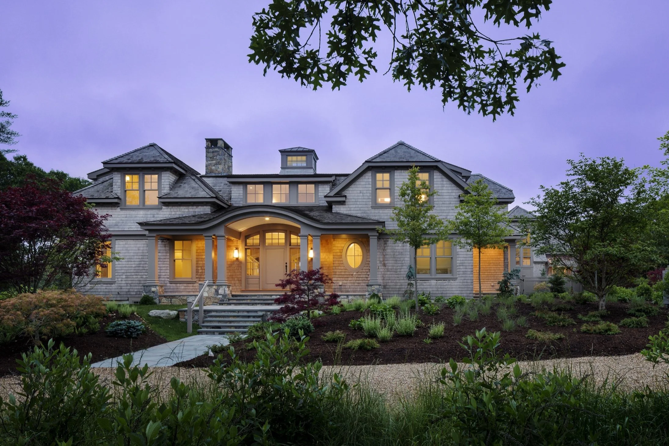 A large, elegant house with a well-maintained front yard, illuminated windows, and a welcoming entrance during dusk.