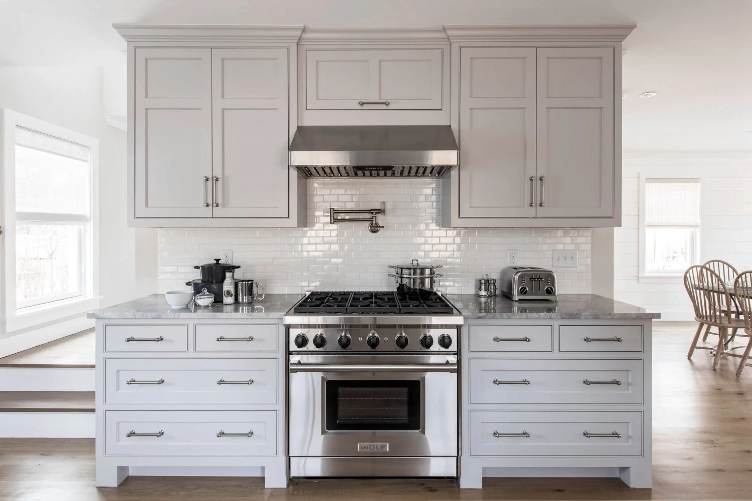 Modern kitchen with white cabinetry, stainless steel stove and oven, white subway tile backsplash, and small appliances on the countertop.