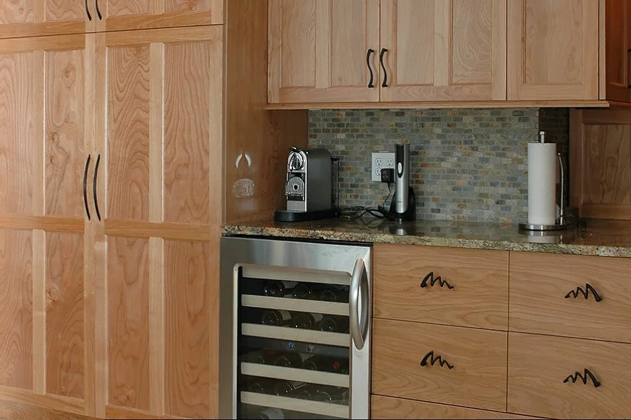 Kitchen countertop with a coffee machine, a cordless vacuum, and paper towel holder, surrounded by wooden cabinets.