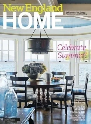 A dining room with large windows overlooking the water, a round wooden table with a vase of flowers, and four black chairs.