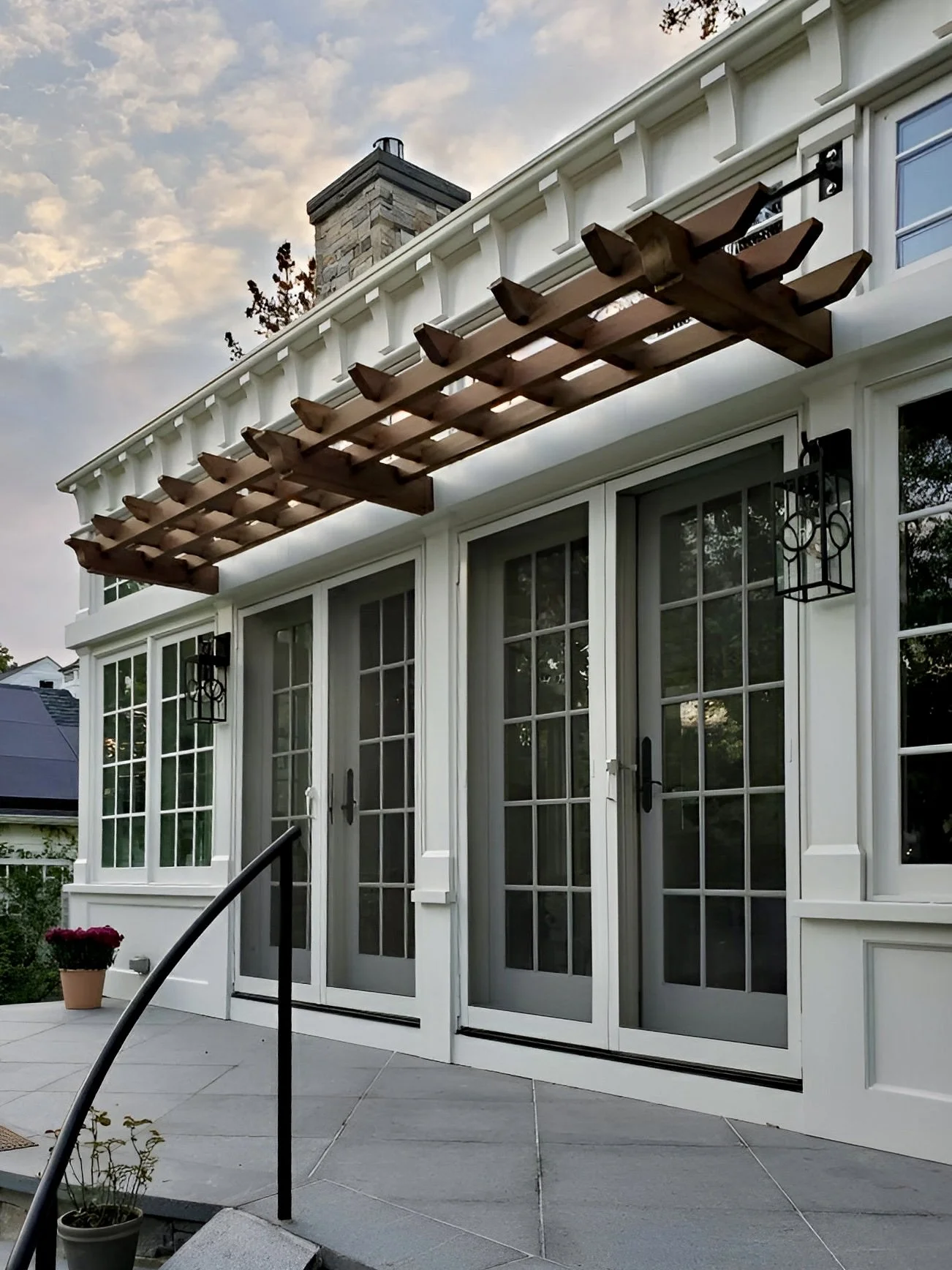 Back porch with white walls, large glass doors, black lantern-style wall sconces, and a wooden pergola above.