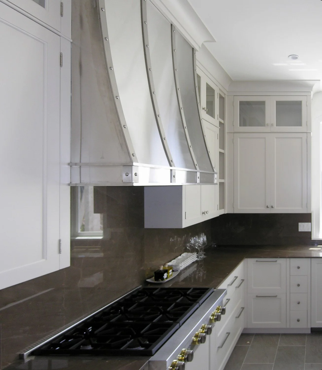 Kitchen with white cabinets, black countertop, stovetop, and stainless steel range hood.