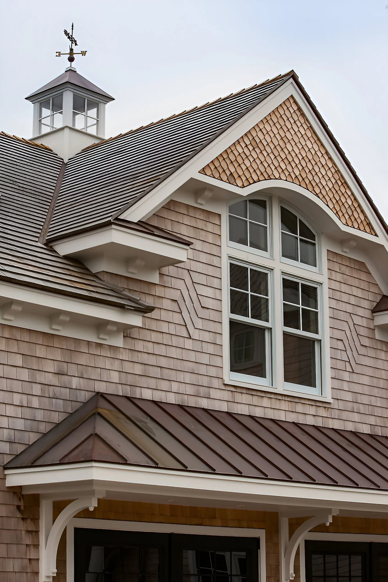 Close-up of a house's upper floor showing a large window, shingle siding, and a roof with a cupola and weather vane.