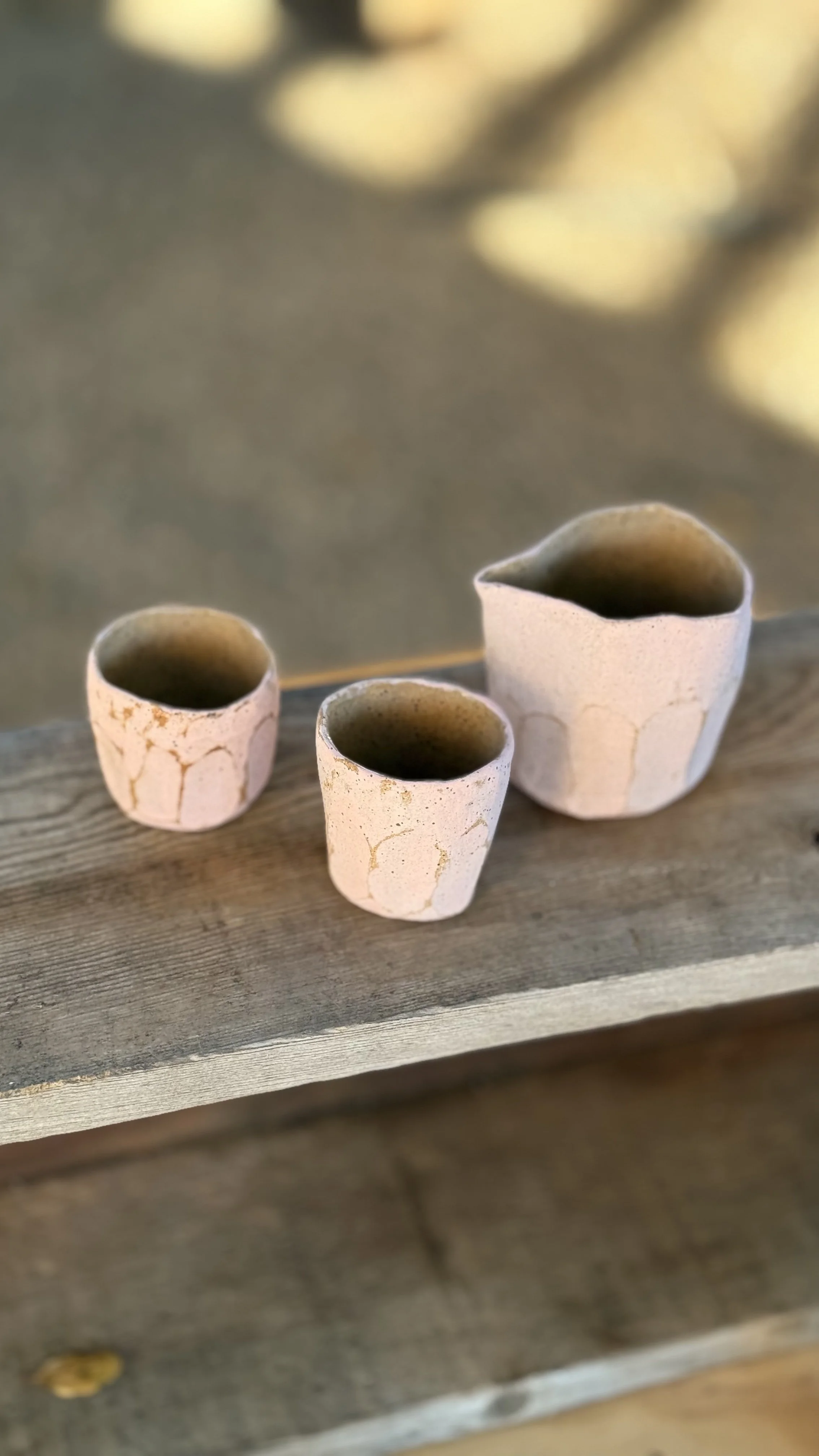 Three small ceramic cups with a crackled white glaze on a weathered wooden surface, filled with a dark liquid.