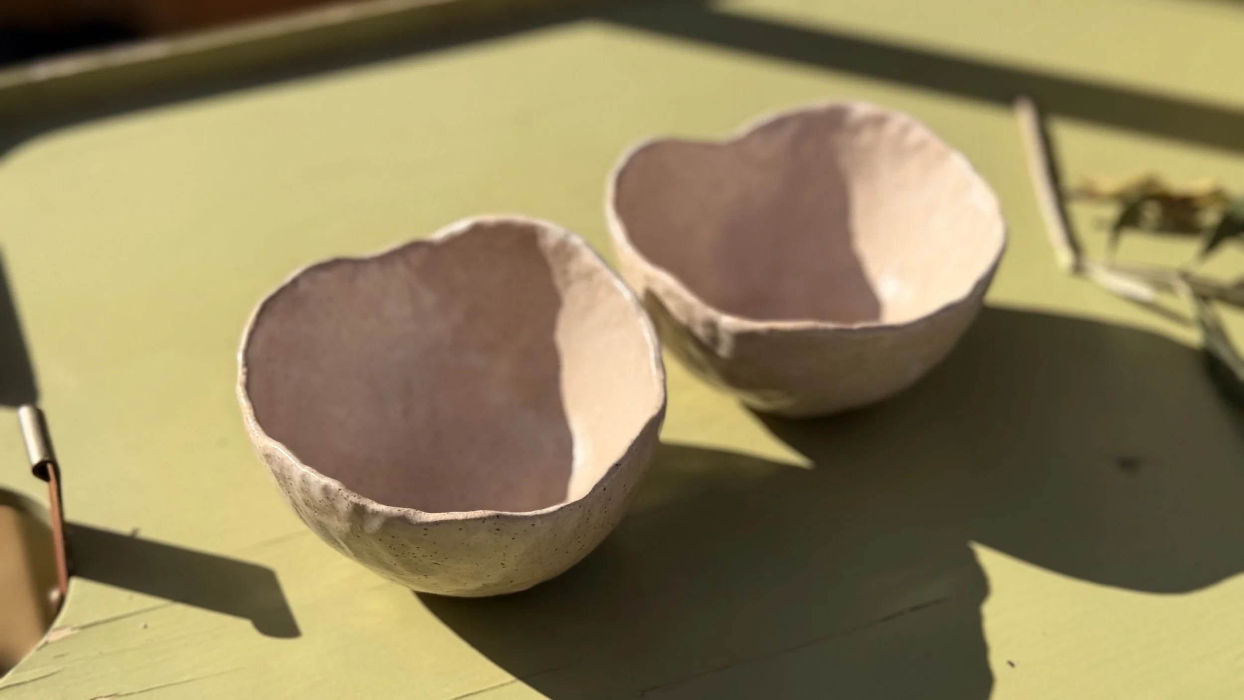 Two small, empty halves of an eggshell with a textured surface, placed on a yellow surface with shadows cast beside them.