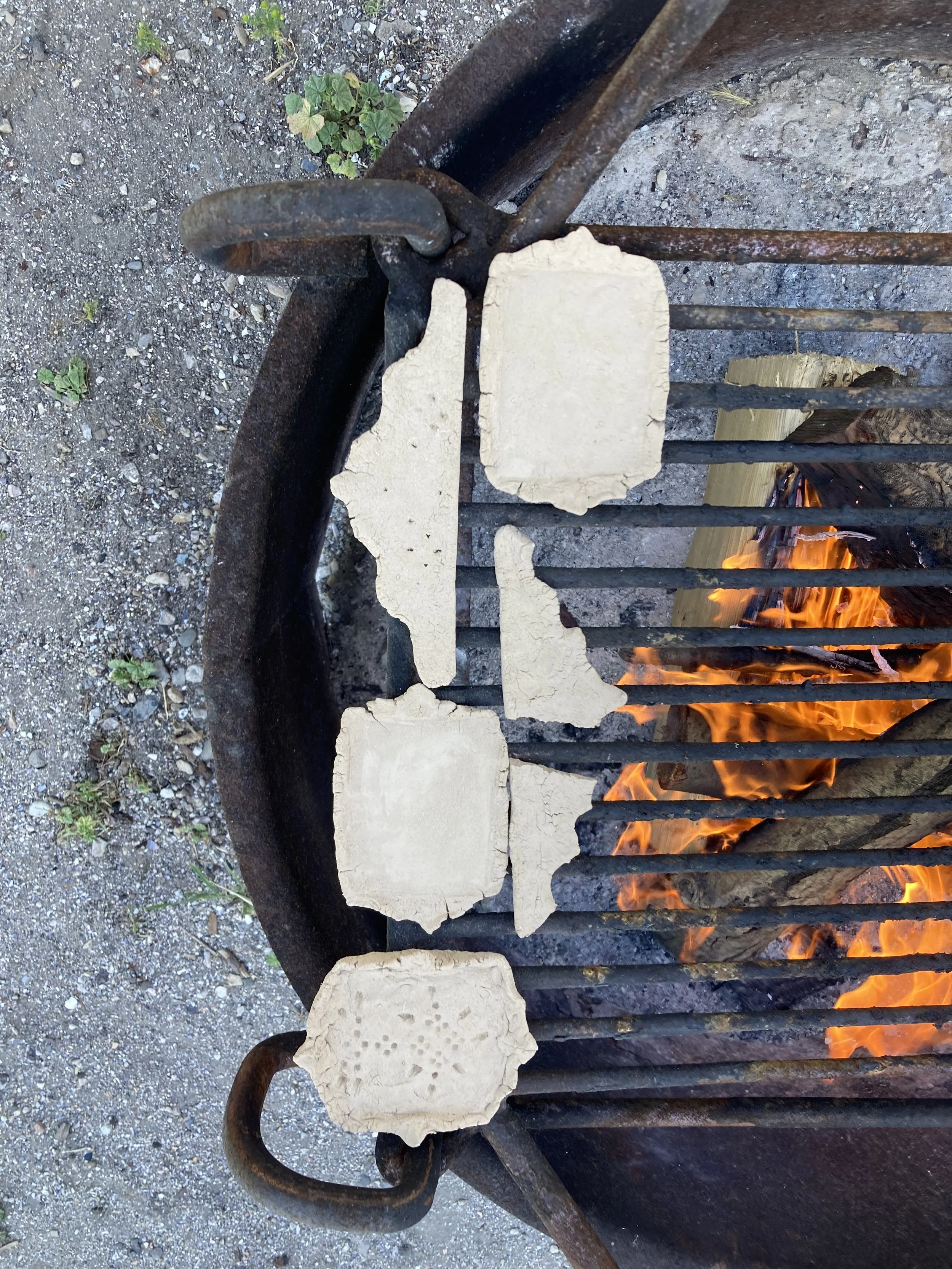 Wild clay drying slowly over a campfire building coals to prepare for the final firing.