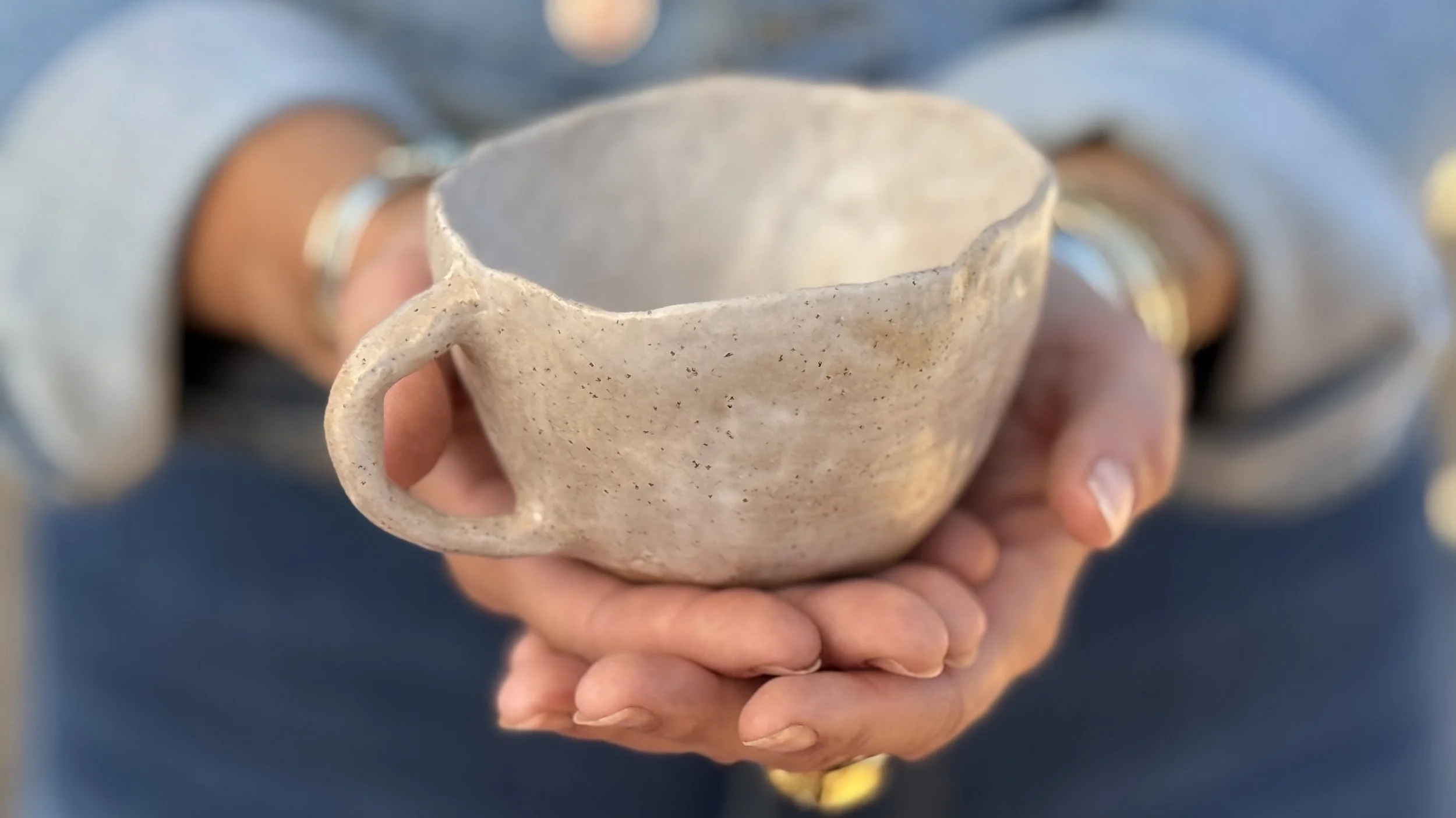 A person holding a handmade ceramic mug with both hands.