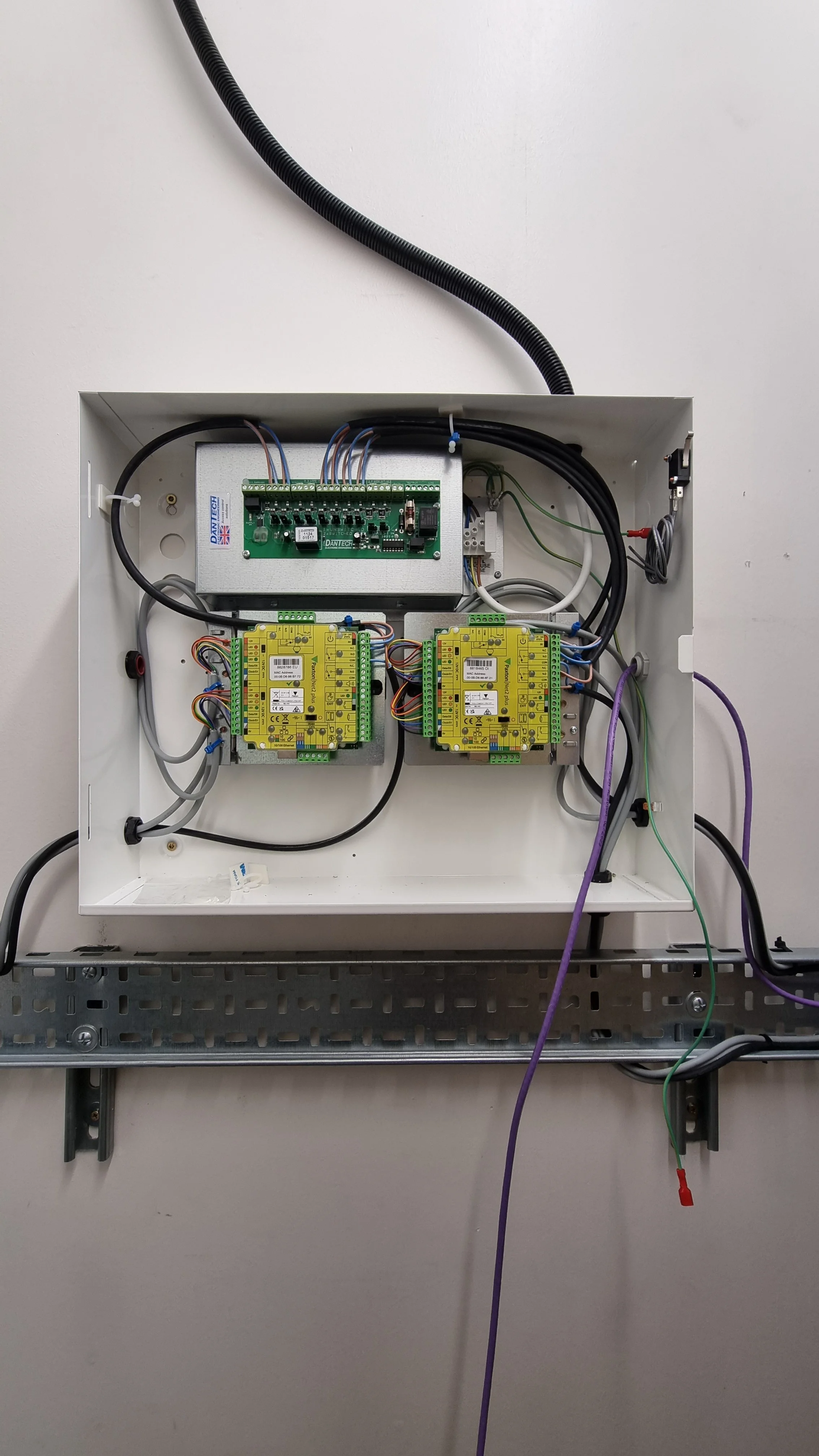 Open electrical control panel with circuit boards, wiring, and components mounted inside a white metal box.