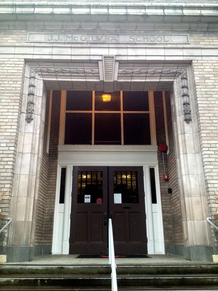 Entrance to J.J. McGlyvr School with dark double doors, brick walls, decorative stone framing, and a sign above reading 'J.J. McGlyvr School'.