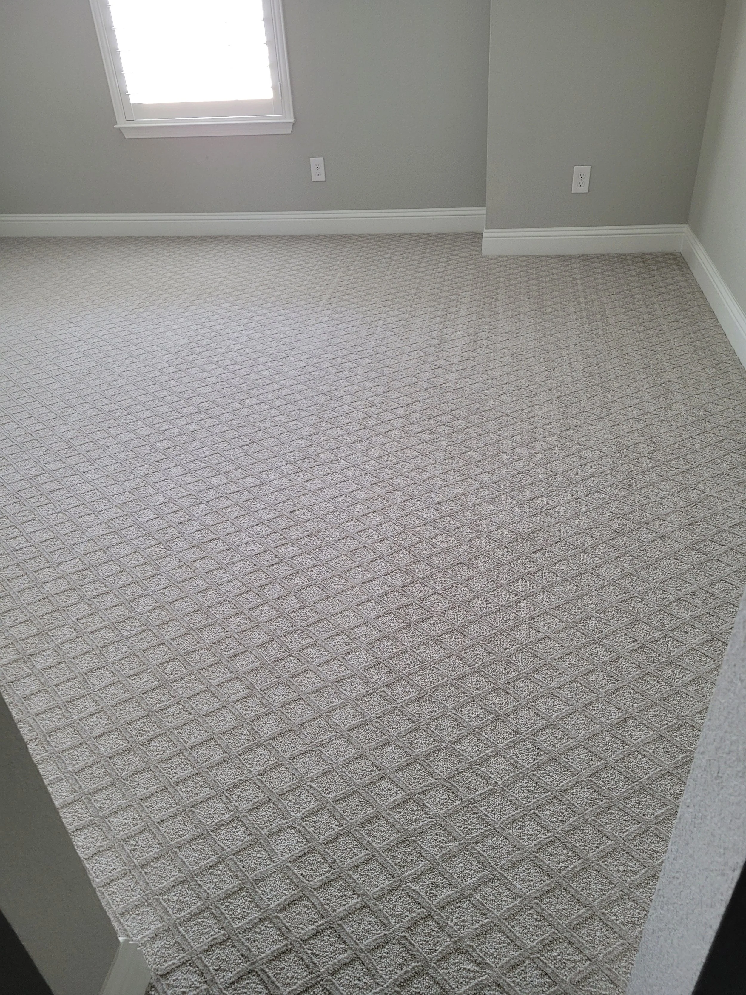 Empty room with gray patterned carpet, a window, and gray walls with white trim.