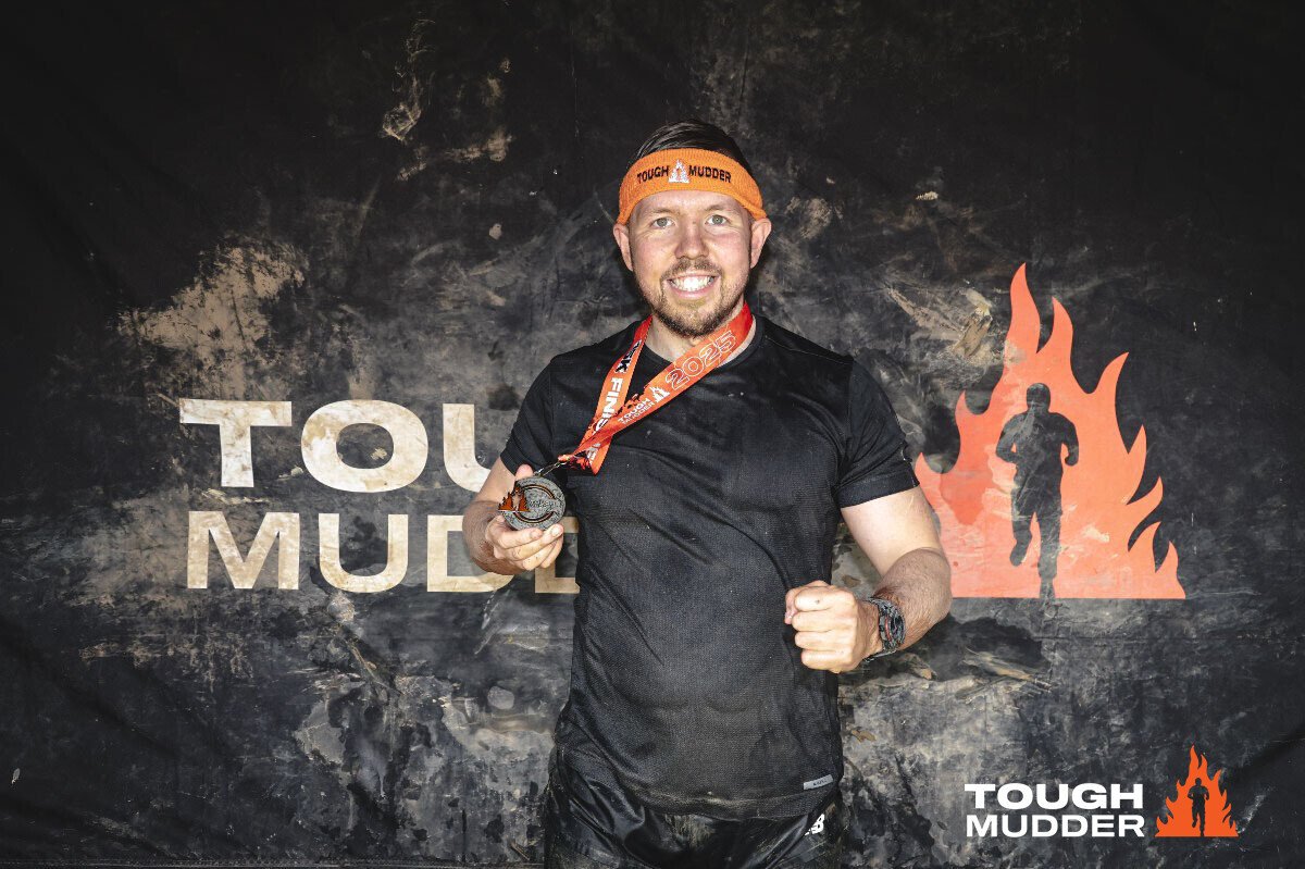 Adam Abel stood in front of a TOUGH MUDDER sign after completing the 15k race in 1:59:00