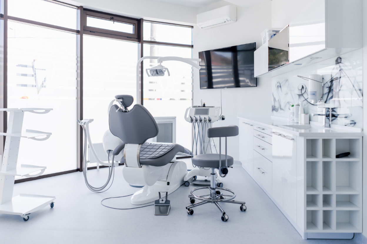 A modern dental clinic room with a dental chair, medical equipment, a television, and storage cabinets.