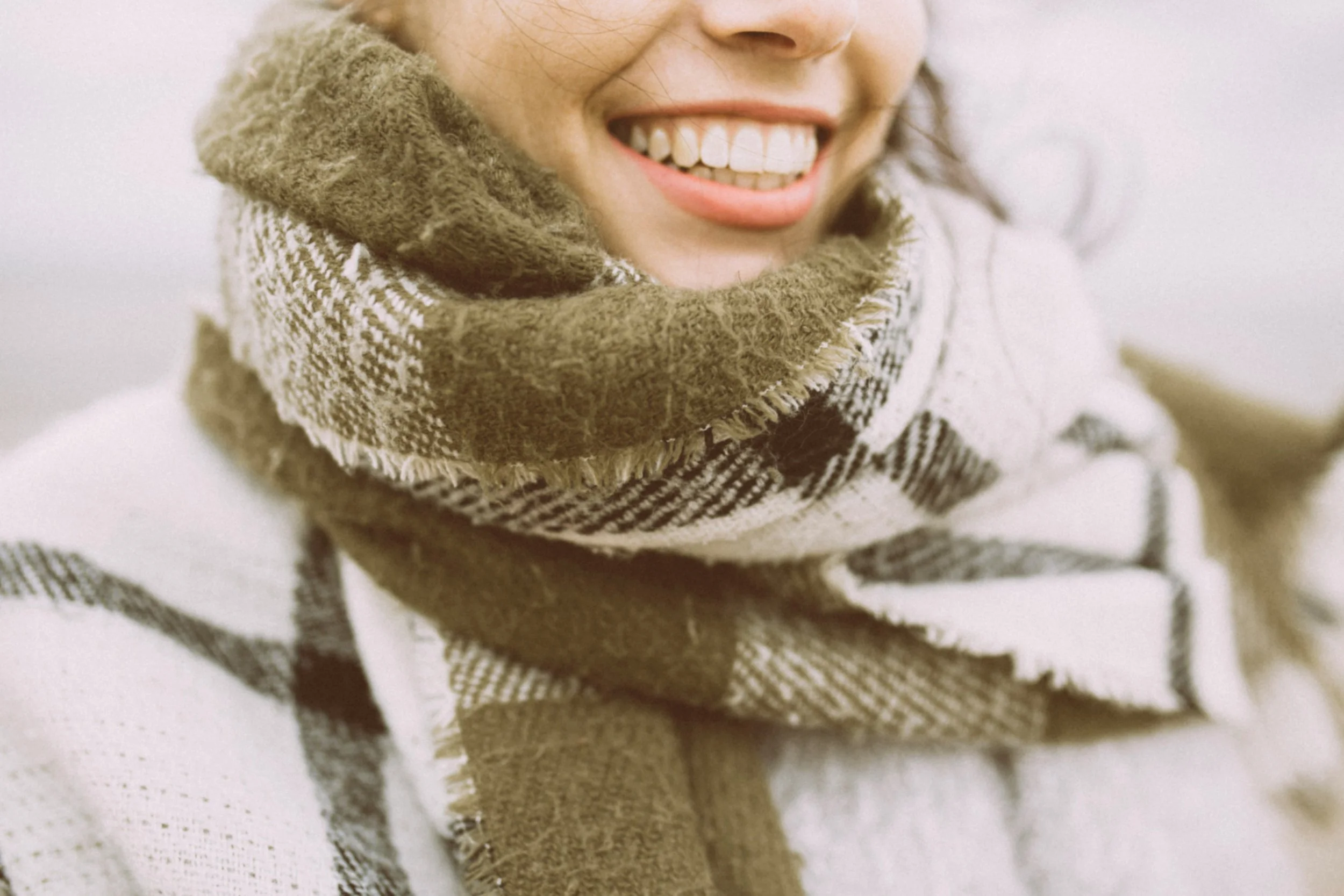 Close-up of a person smiling in a warm scarf, illustrating winter comfort and cold-weather tips for protecting orthodontic retainers.