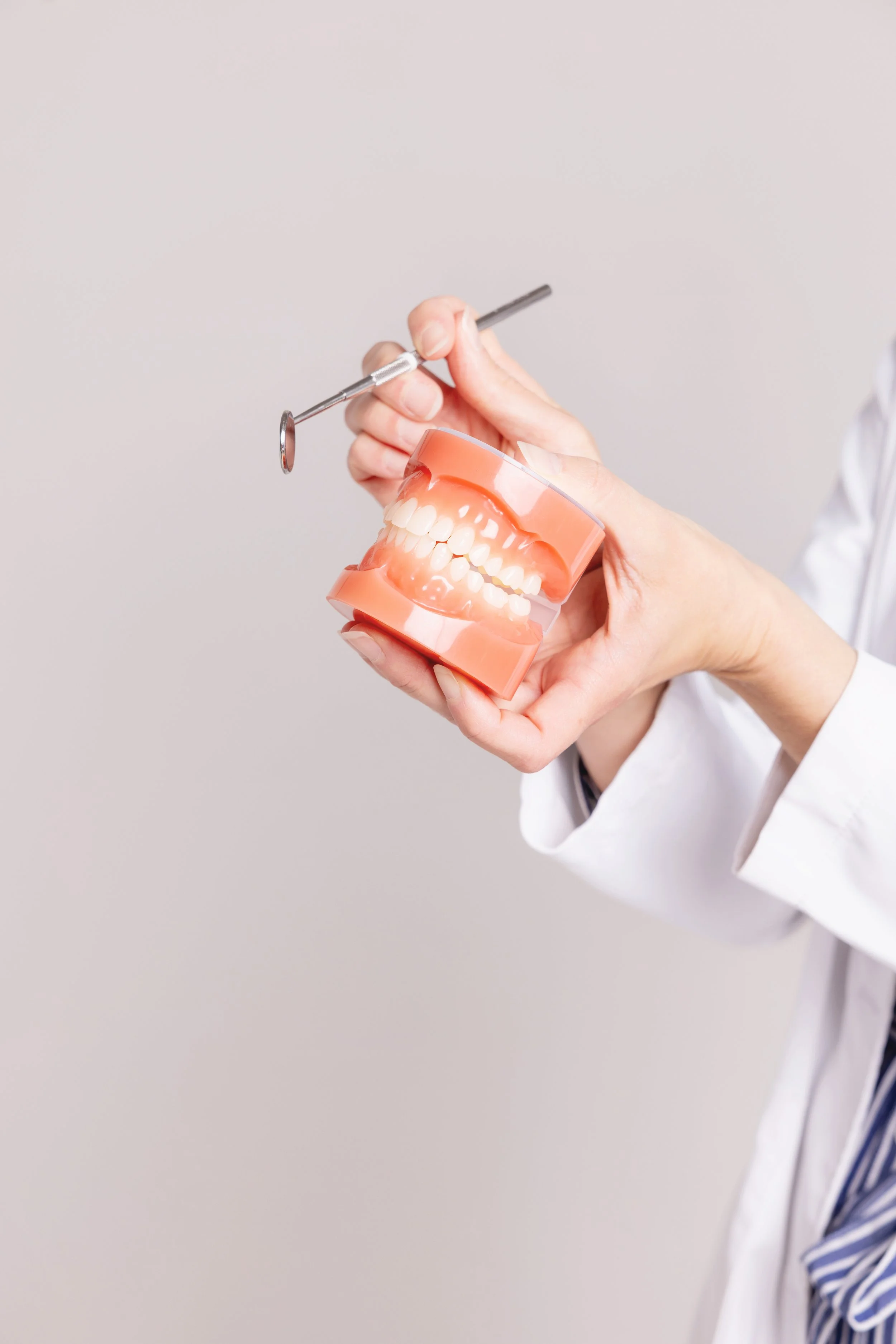 Orthodontic professional holding a dental model and mirror to demonstrate proper retainer fit and care during colder months.